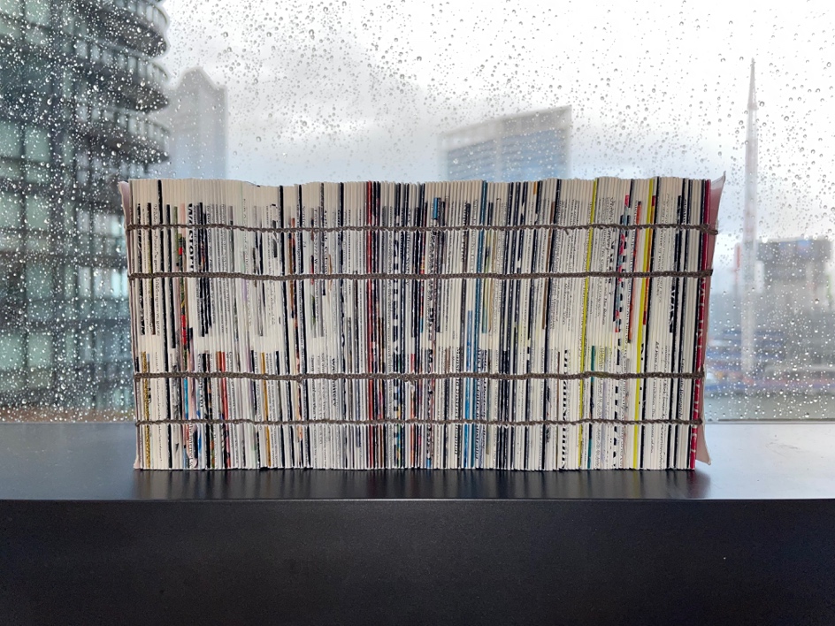 A handmade concertina artist's book with visible stitching and colorful pages, placed on a black surface with a rainy window and cityscape in the background.