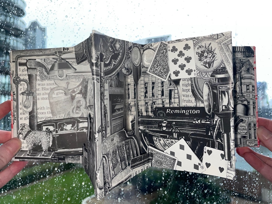 An open artist's book featuring intricate black-and-white collage elements, held in hands against a rainy window backdrop.