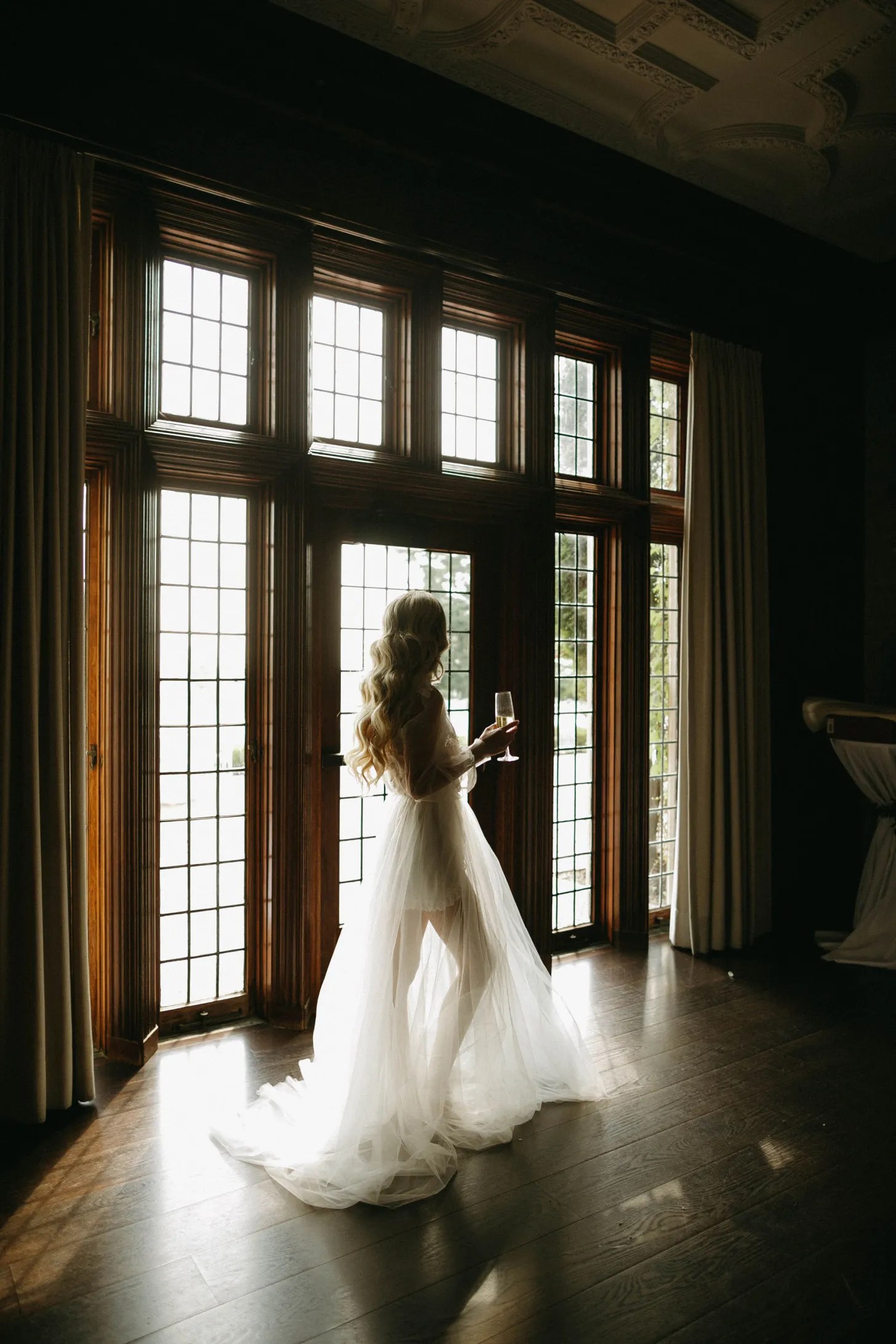 bride standing in the frame of a large set of windows in her getting ready attire the morning of her ceremony