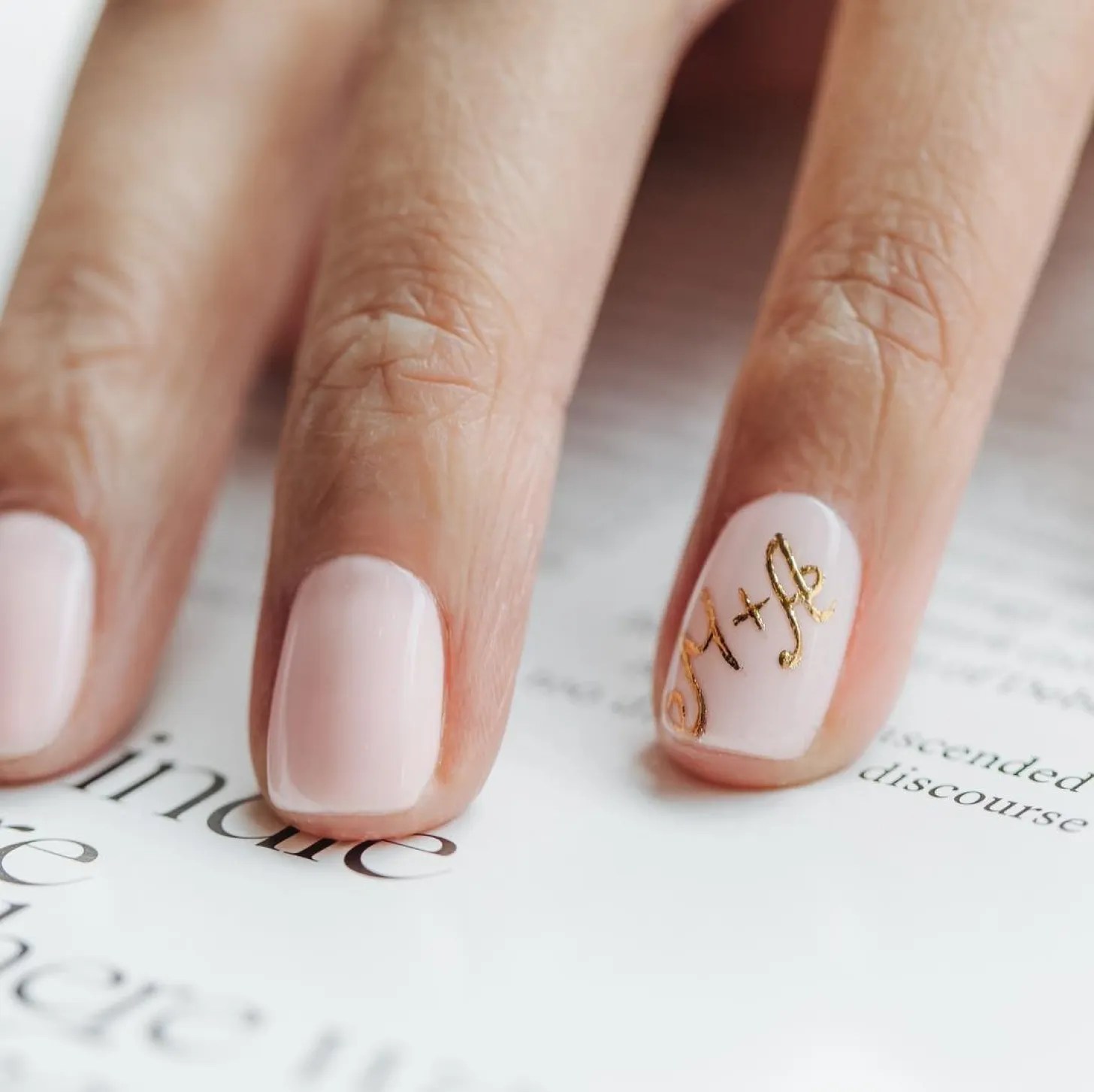 custom blush manicure with gold M+A initials drawn onto the ring finger
