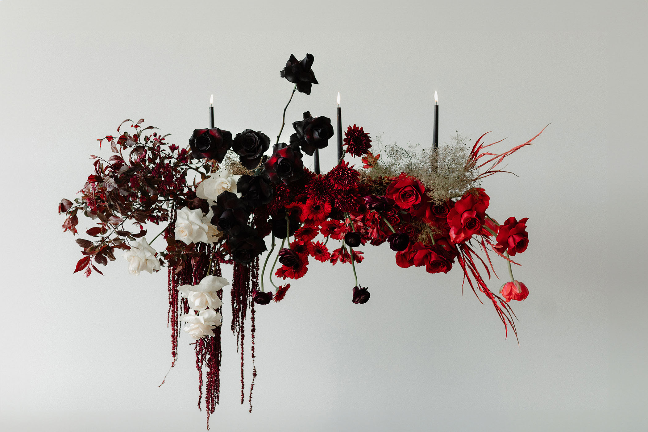 a black and red asymmetrical floral arrangement with black candlesticks protruding from it