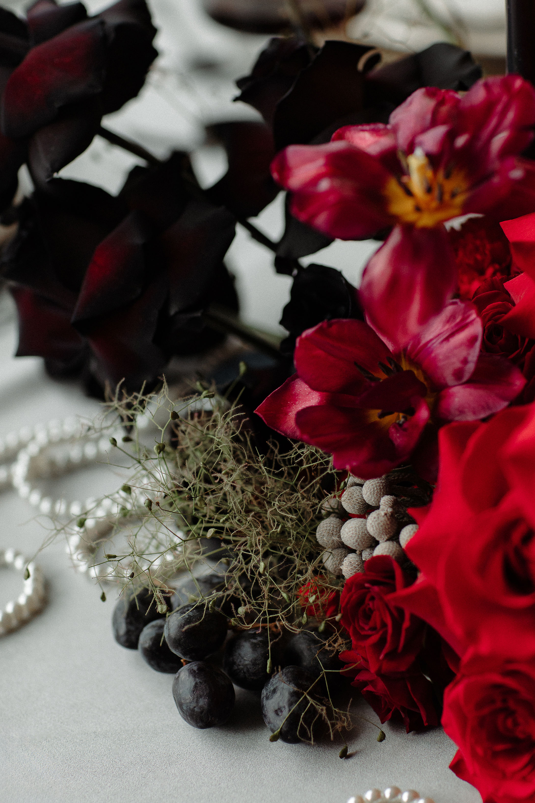 close up of a red floral arrangement with pearl necklaces strewn in the background