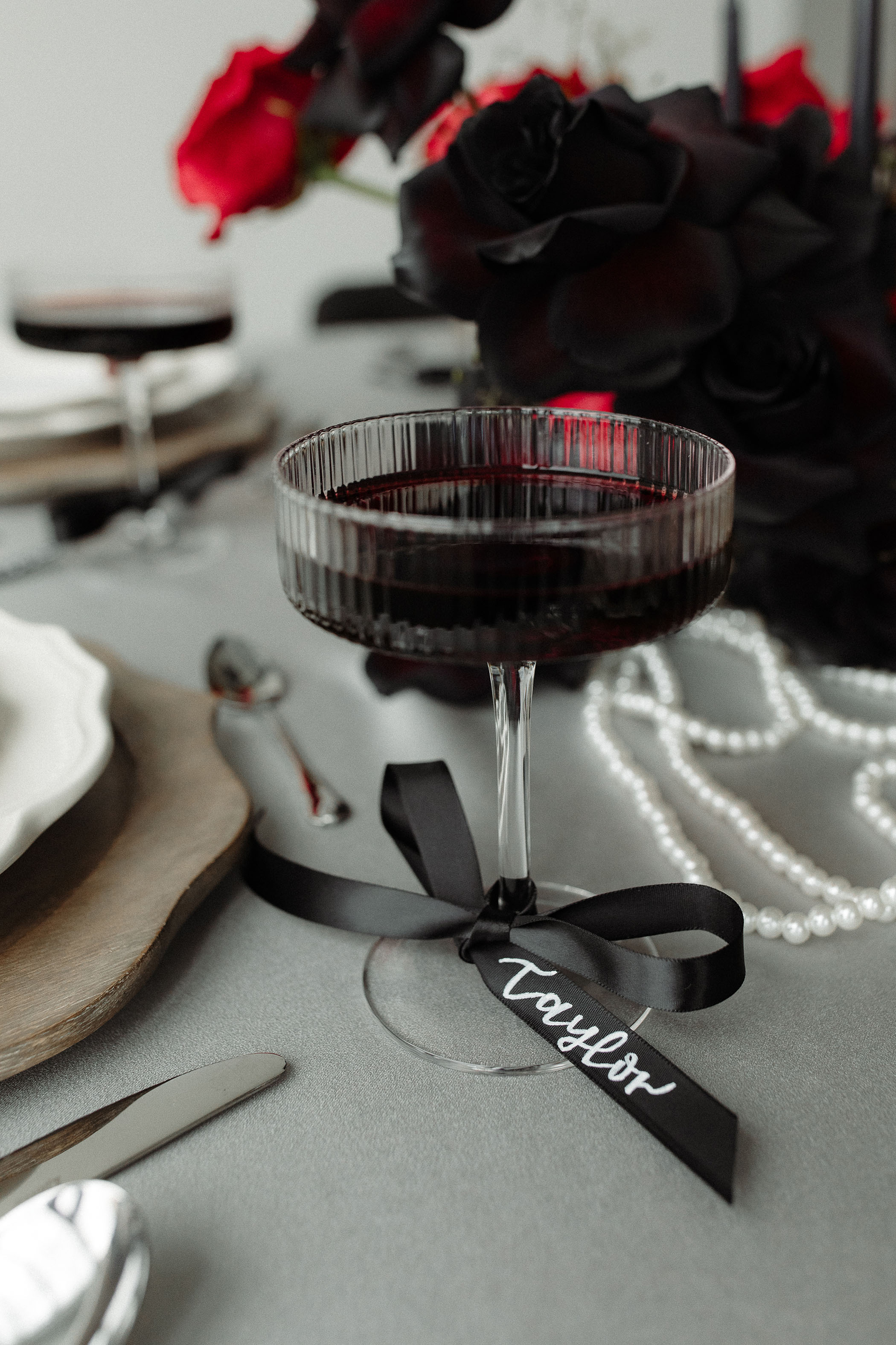 a wine glass with a black bow tied around it with the name Taylor written on it for a Tortured Poets Department wedding photoshoot