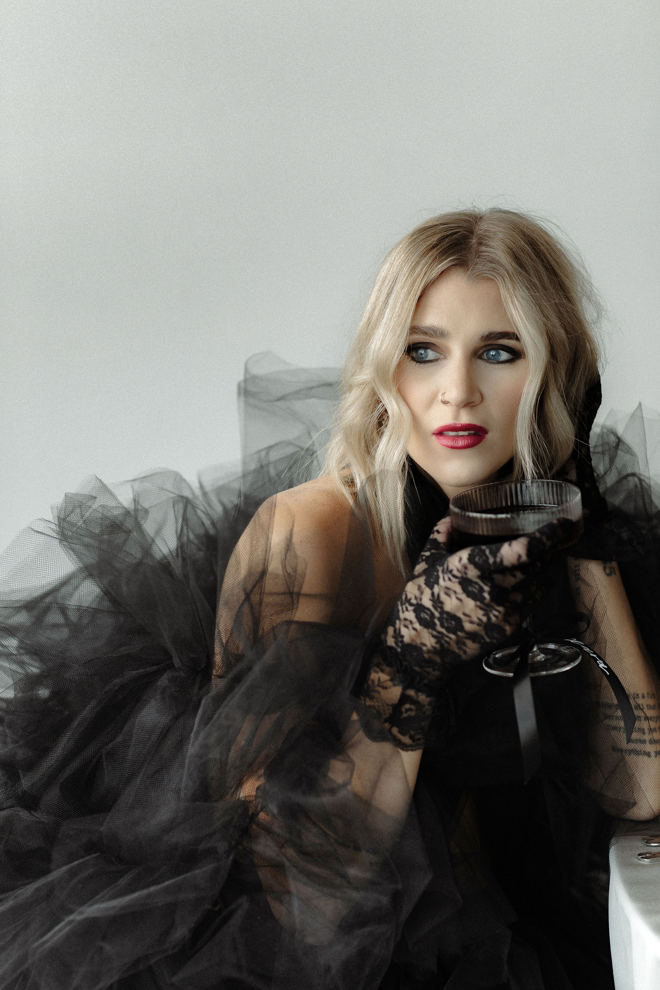 woman in a poofy black tulle dress with vintage lace black gloves and red lipstick drinking a glass of wine in a TTPD inspired photoshoot