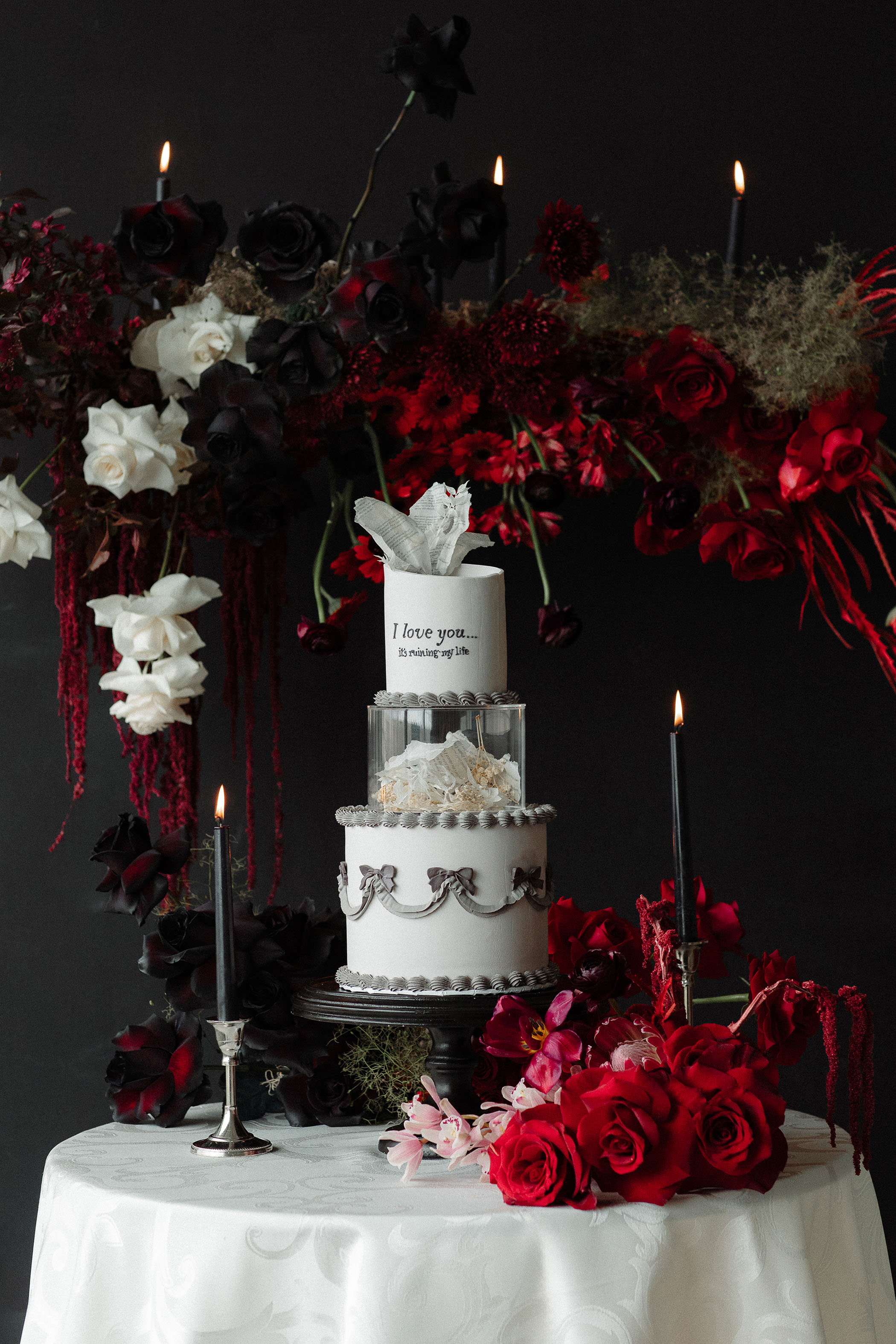 three tier Tortured Poets Department photoshoot wedding cake with gray bows referencing Clara Bow and writing on the top tier that says "I love you...it's ruining my life" referencing the song Fortnight on Taylor Swift's TTPD album