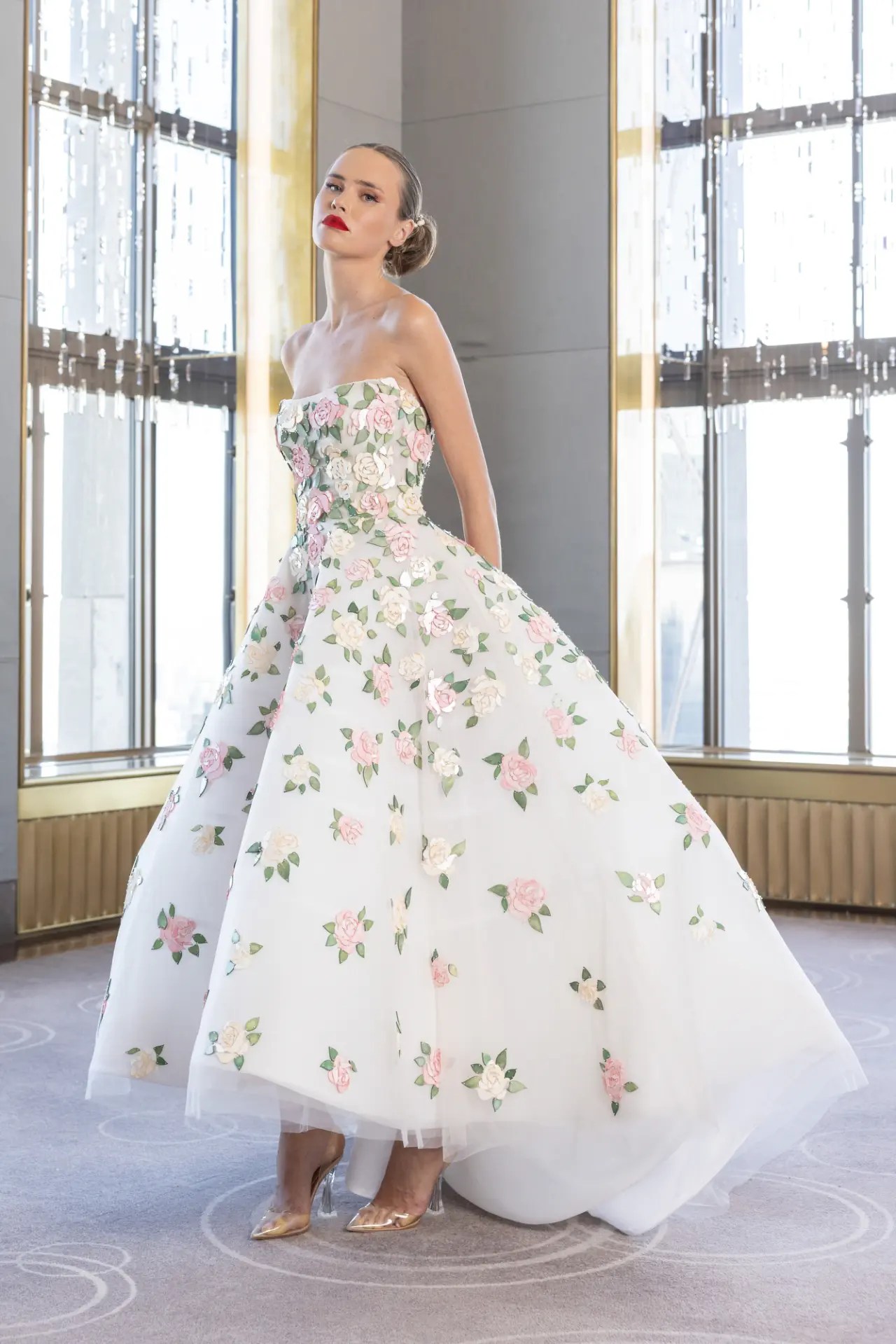 Nardos Spring 2027 strapless white ball gown covered in dimensional pink and cream rose appliqués with green leaf accents across the full skirt and bodice, styled with gold heels, shown at New York Bridal Fashion Week.