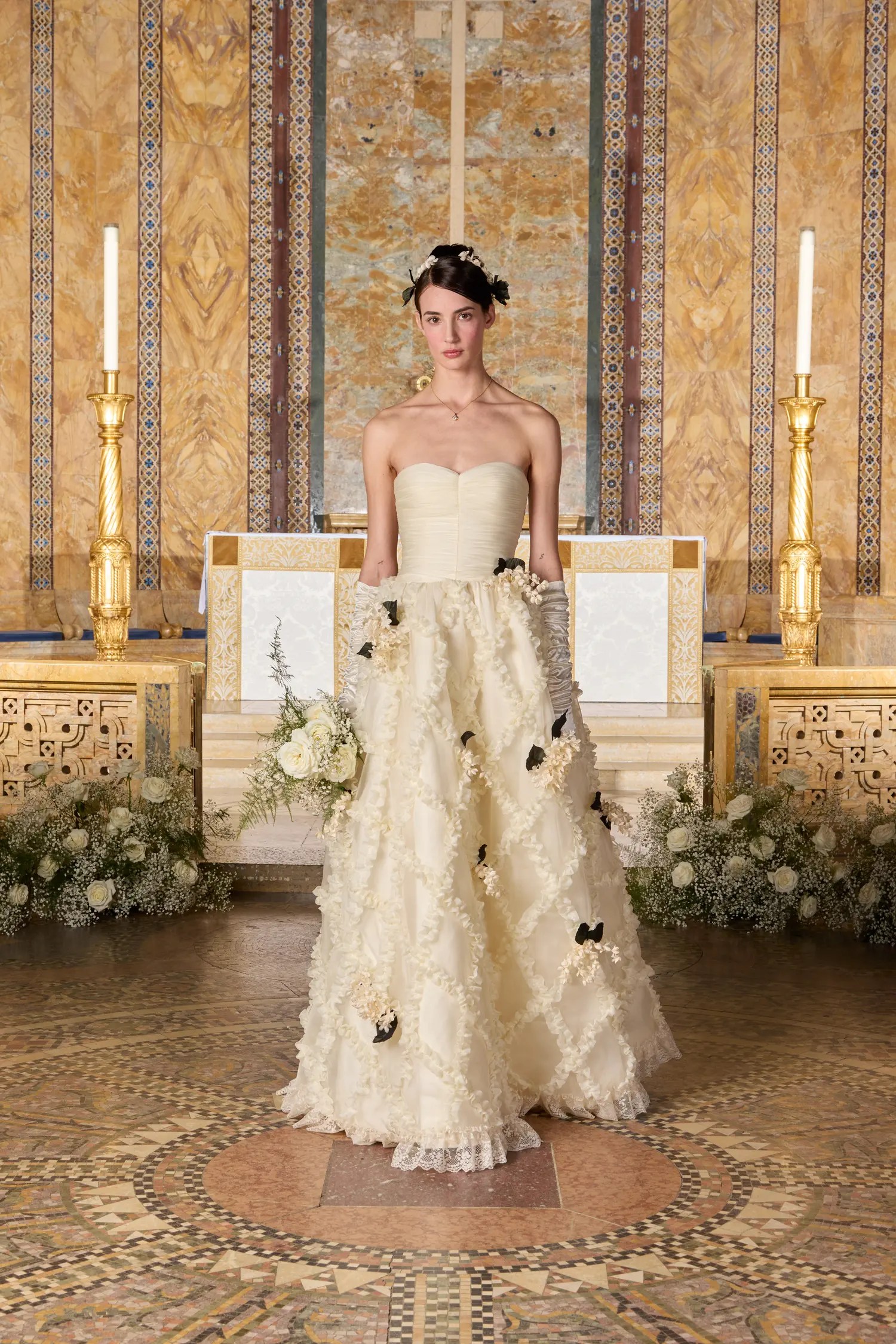 Tanner Fletcher Spring 2027 strapless sweetheart ball gown with ruched bodice, textured floral skirt with scattered black flower accents, paired with long gray gloves and a dark floral headpiece, shown at New York Bridal Fashion Week.