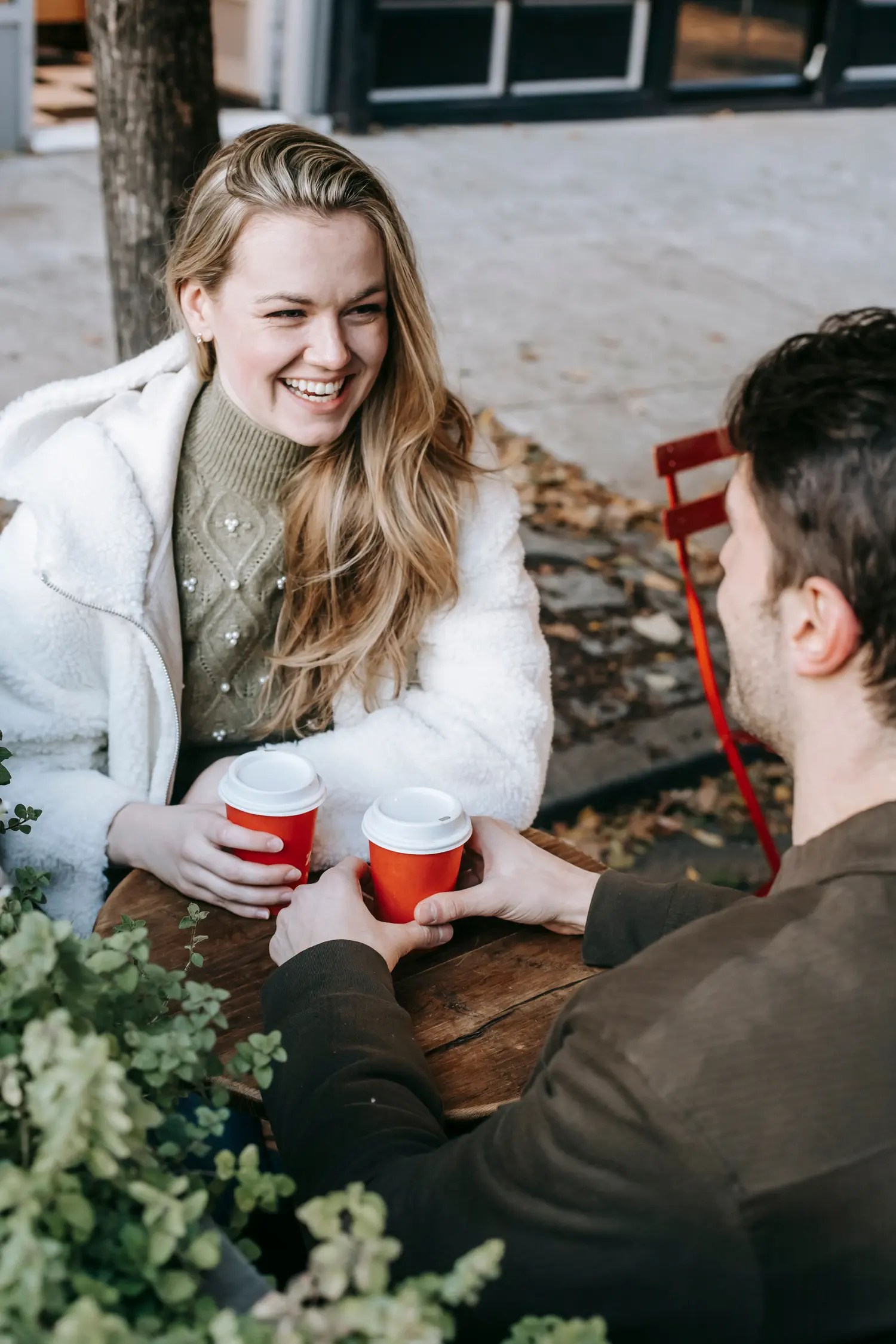 Smiling woman in a white coat talking with a man over coffee at an outdoor cafe table on a first date