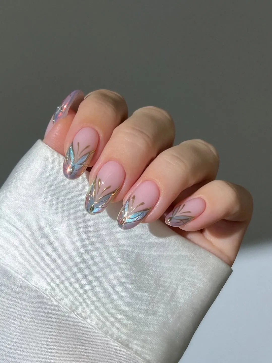 Butterfly French tip nails in iridescent blue and gold chrome with gilded outlines on a sheer pink base