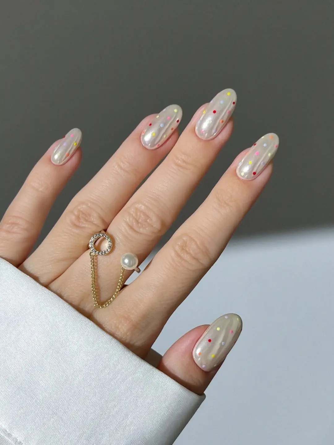 Pearl chrome nails with rainbow microdots in red, lilac, marigold, and pink on long almond nails
