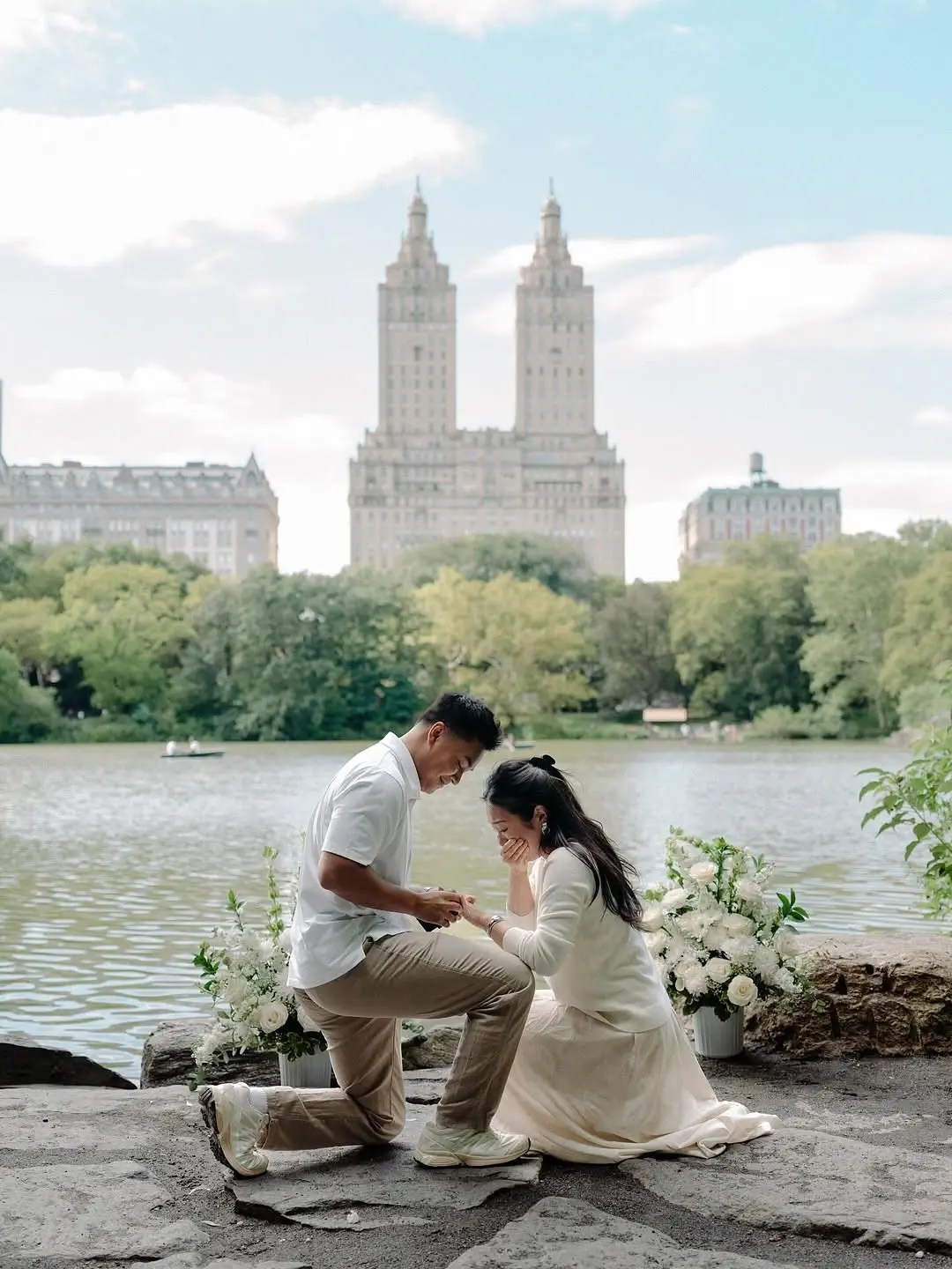 Central Park proposal beside the lake, white floral arrangements framing the couple on the rocks