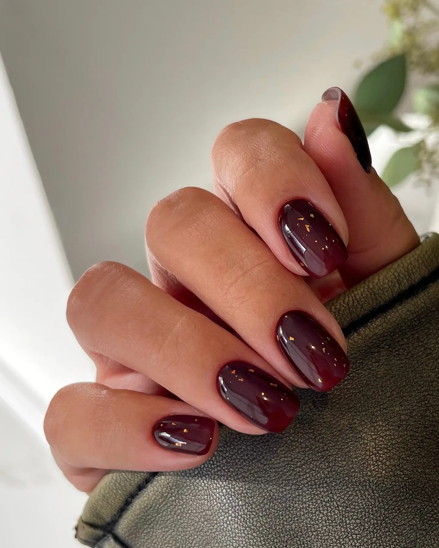 Short fall nails in glossy dark oxblood with scattered gold flakes suspended under the topcoat
