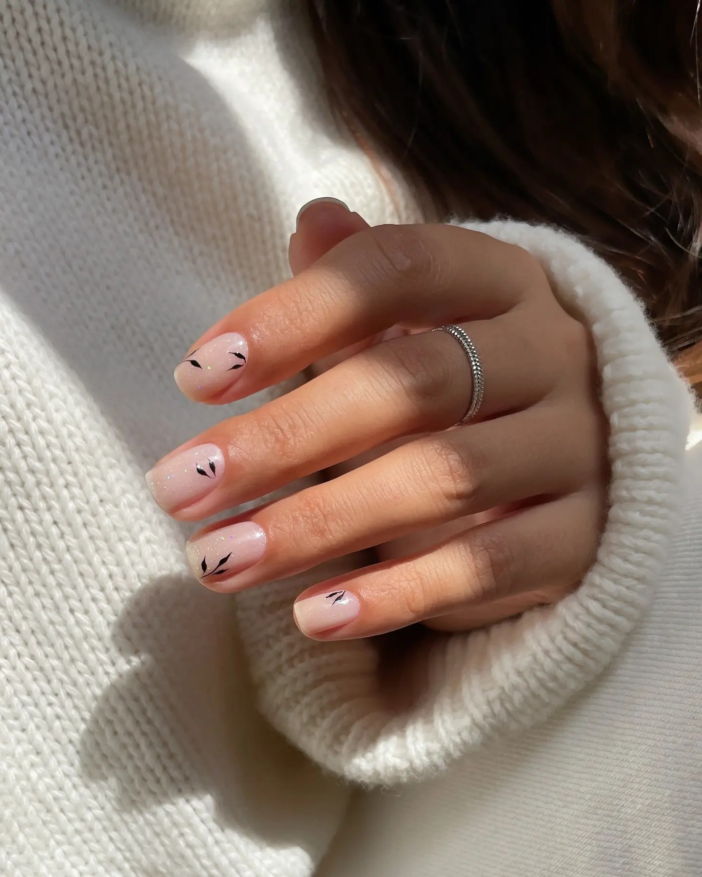 Short fall nails in a sheer shimmery pink with fine black leaf sprigs painted near the cuticle