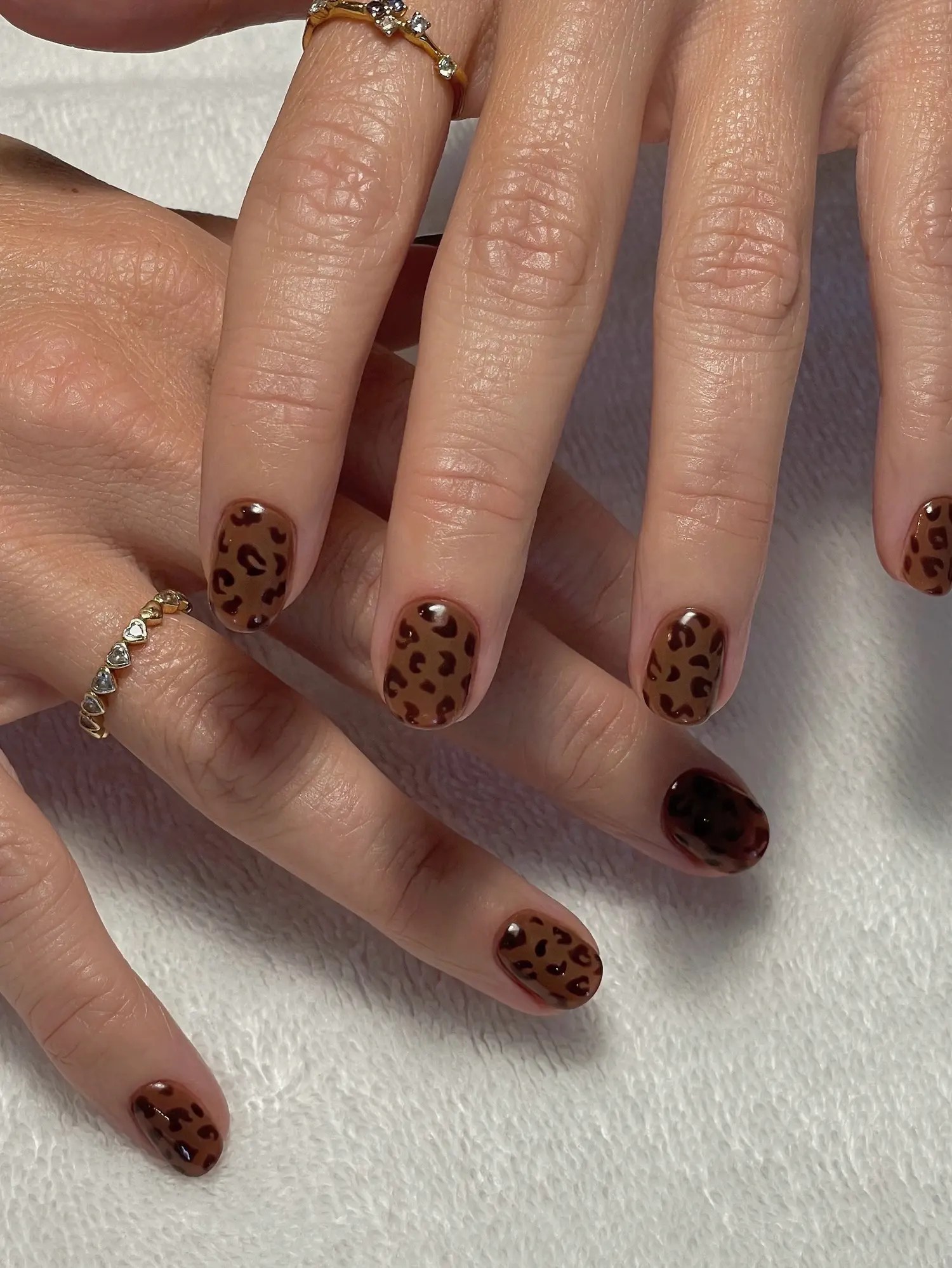 Short oval October nails in caramel with hand-painted espresso leopard spots and one deep mahogany accent nail