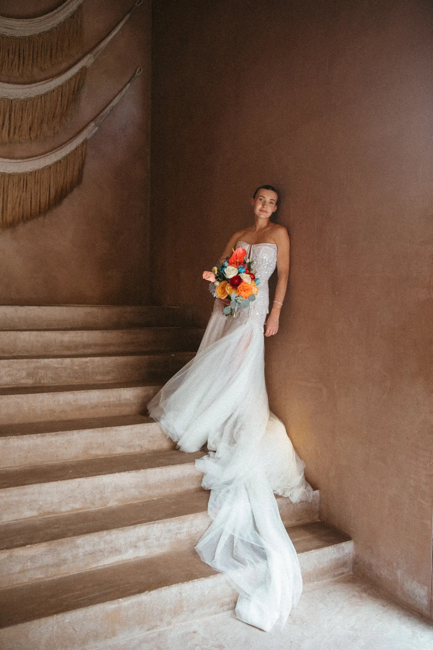 Bride in the Kim Kassas Melisandre gown holding a vivid orange and blue bouquet on a terracotta stone staircase