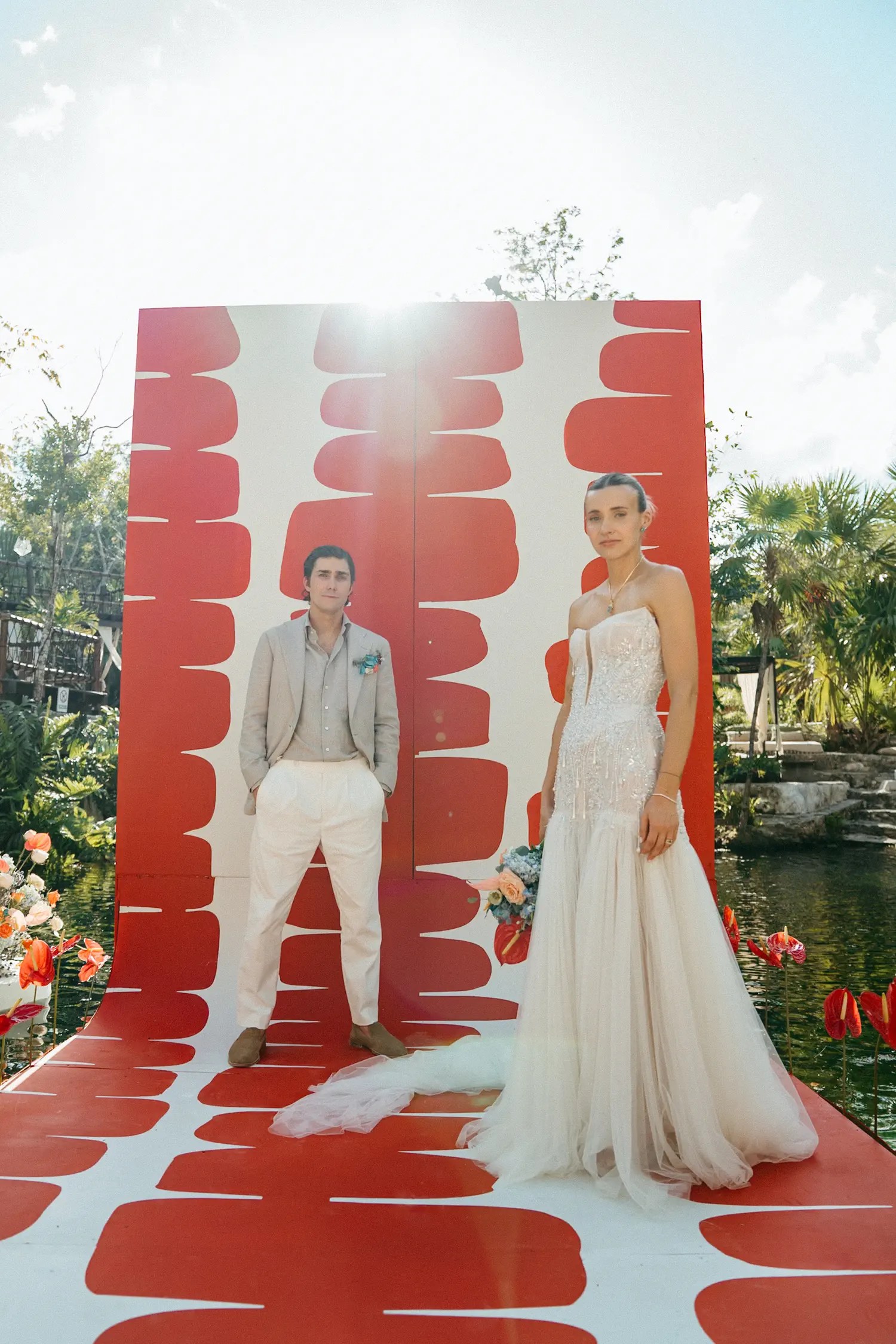 The couple on the ceremony platform in front of the red-and-white backdrop in strong late-day backlight
