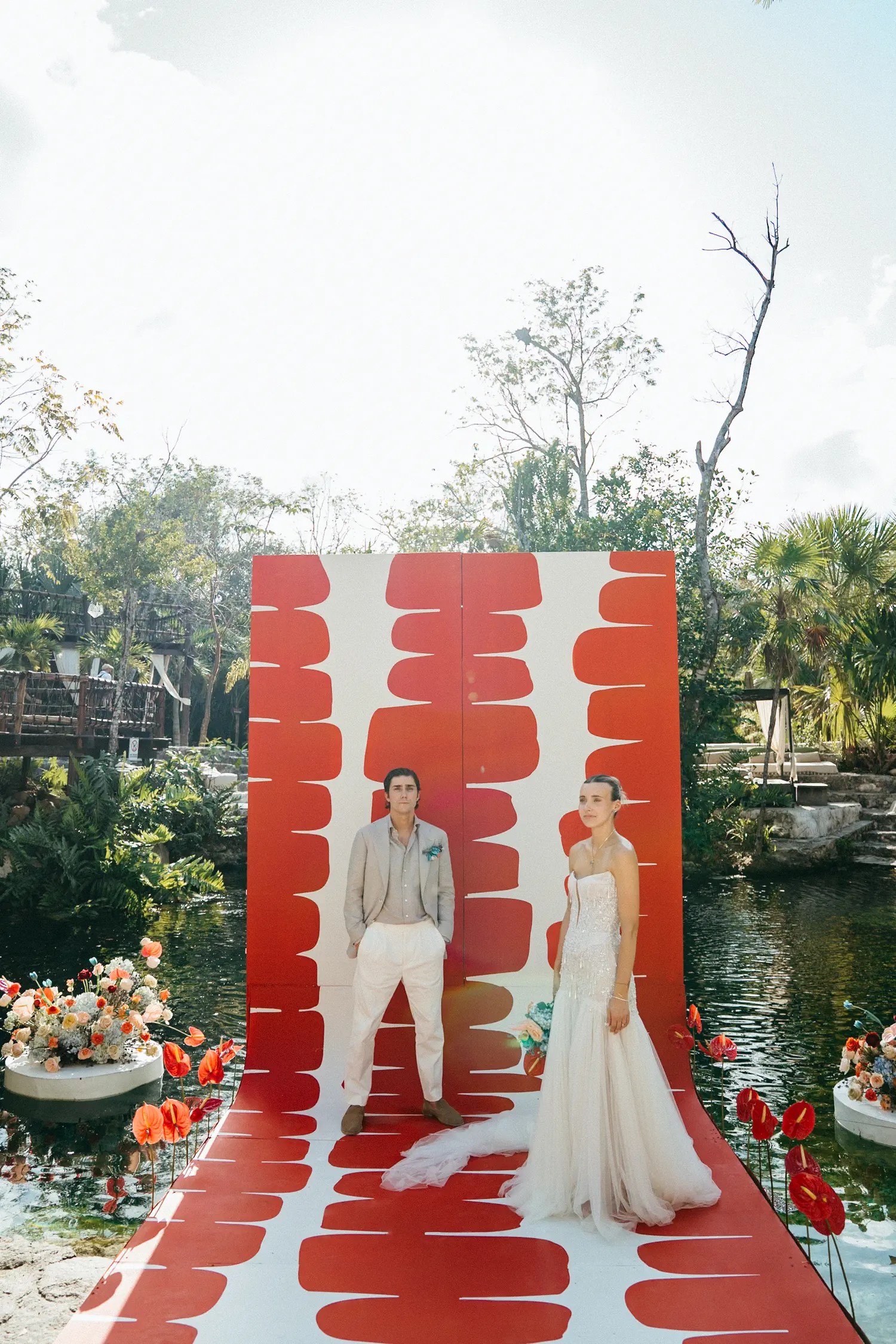 Laura and Stephen standing apart on the patterned ceremony runway with cenote water on both sides