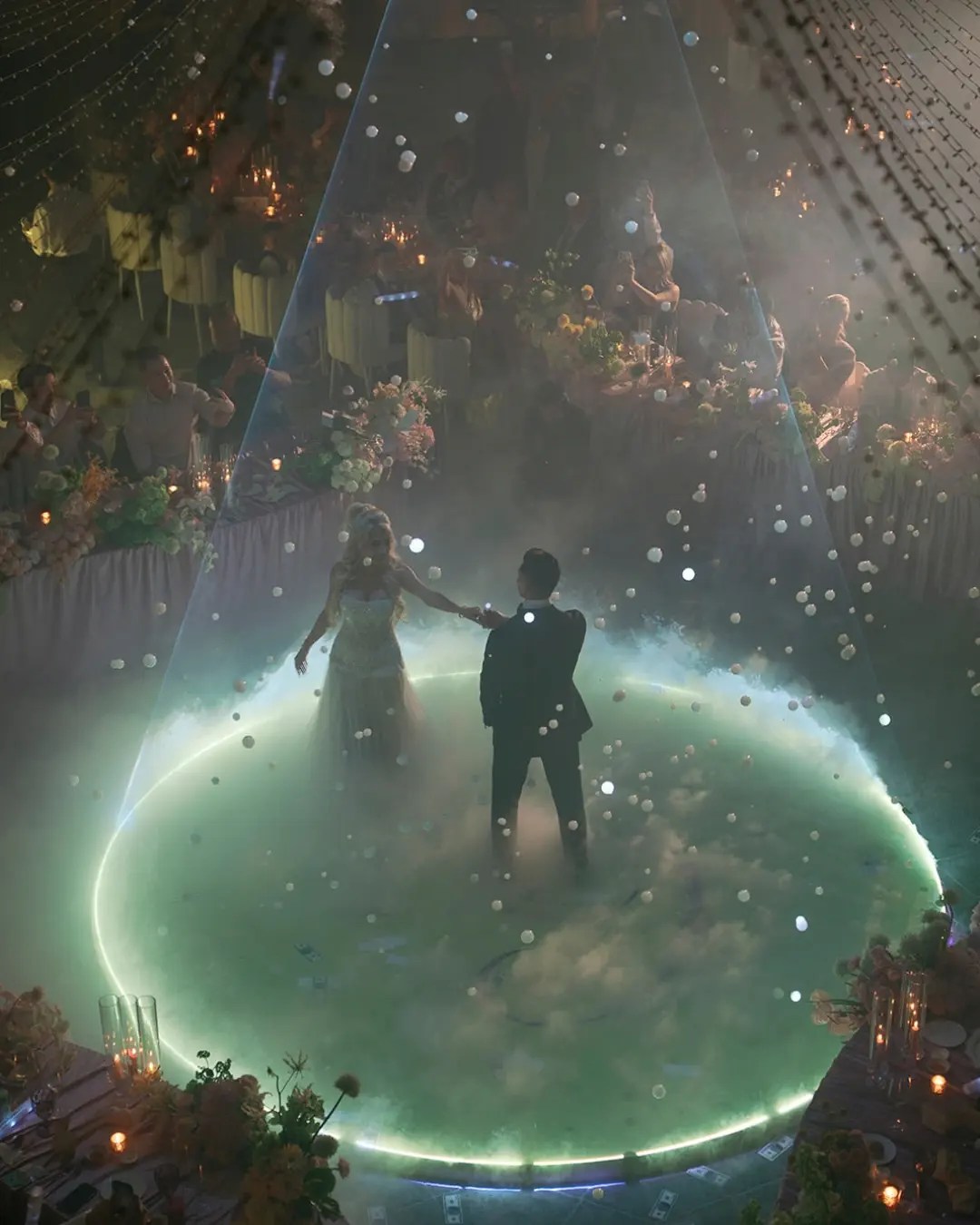 Couple's first dance on a glowing mint-green circular dance floor under strings of lights with low fog