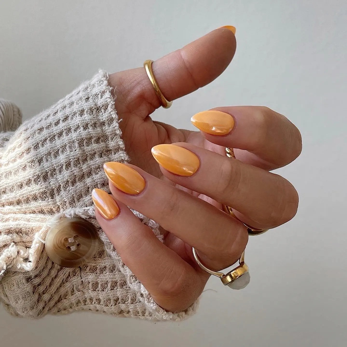 simple glazed pumpkin orange nails on almond nails with gold rings and a cream waffle knit sweater