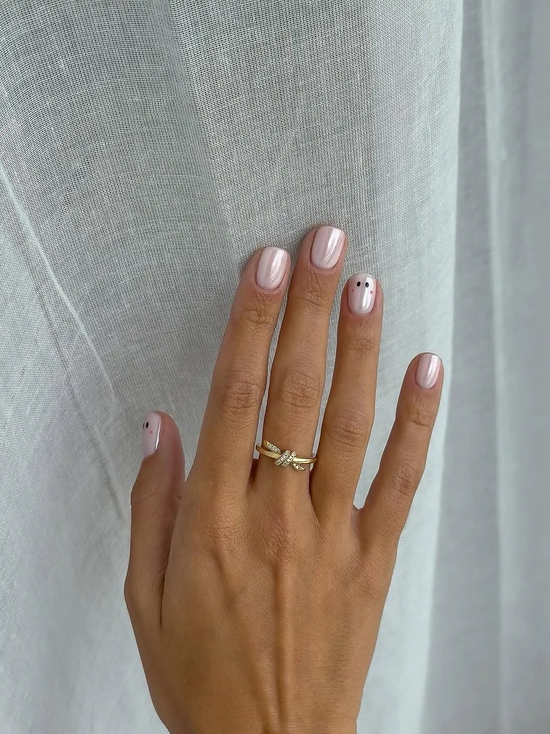 Short square nails in a milky pearl pink with two accent nails each painted with one tiny white ghost with dot eyes and blushed cheeks