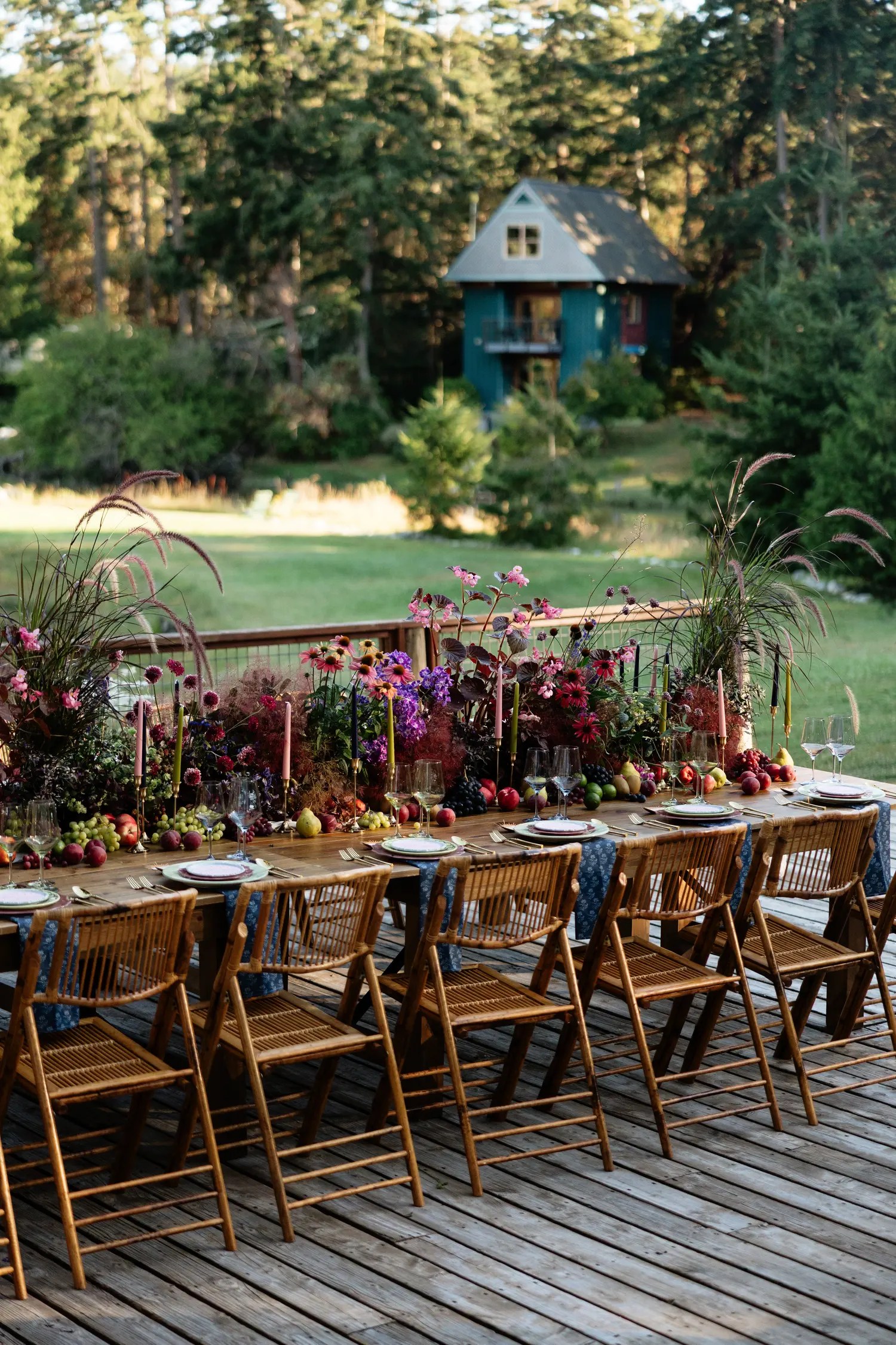 Full-length outdoor wedding reception table with a denim blue printed runner, layered sage and mauve plates, pink menu cards, and a colorful fall floral centerpiece