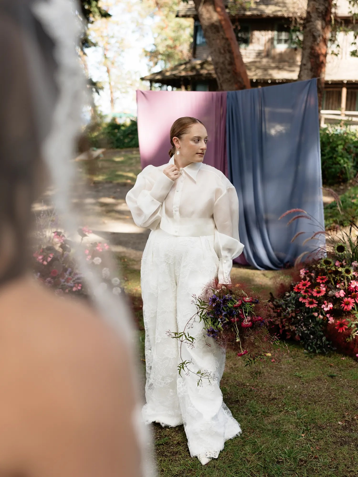 Bride in a sheer organza barong with balloon sleeves, high buttoned collar, white lace wide-leg trousers, and a pearl drop earring, seen through a veil