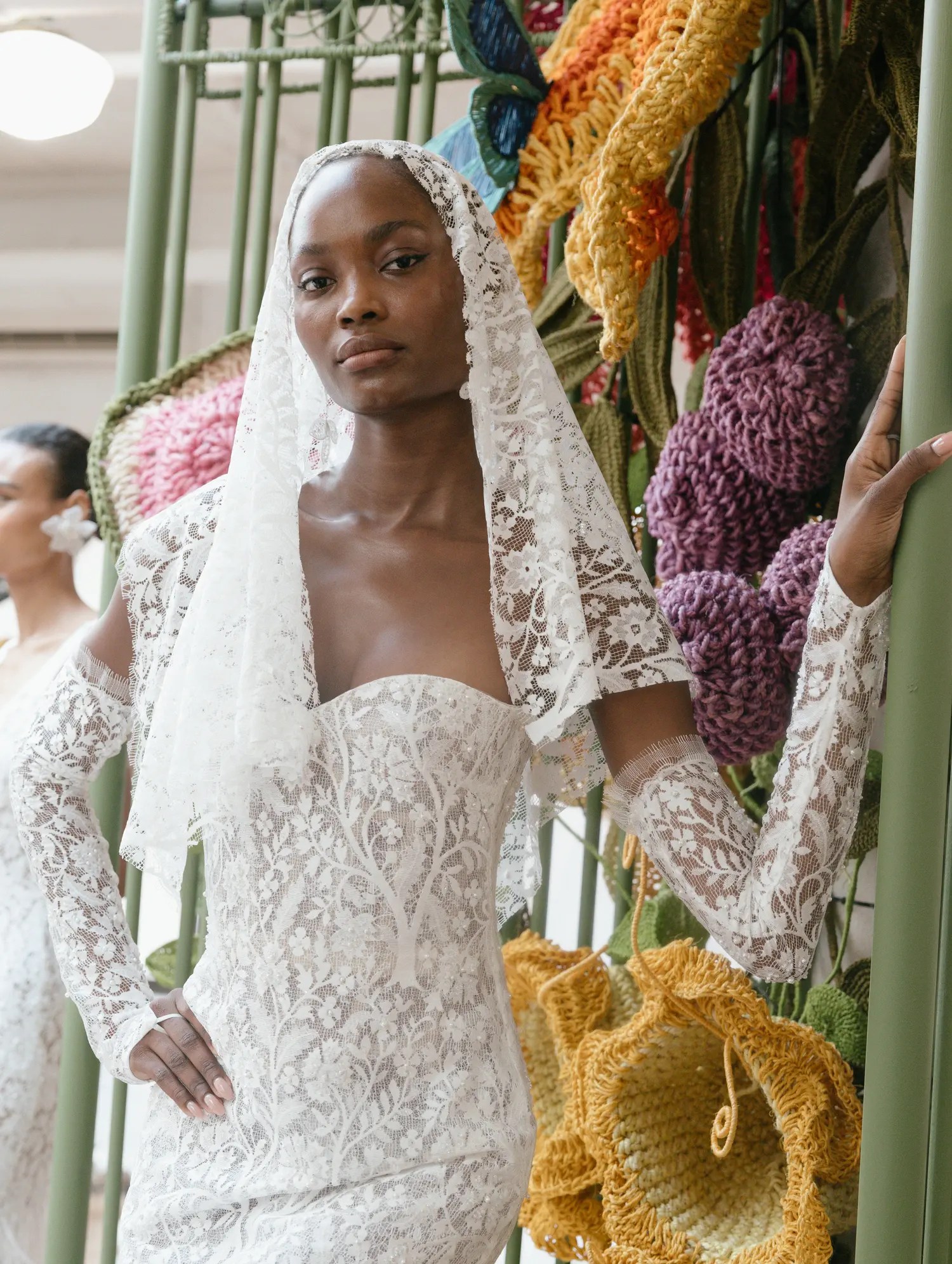 Francesca Miranda lace mermaid wedding dress with a lace mantilla veil, strapless sweetheart bodice, and lace sleeves, beside giant handcrafted flowers