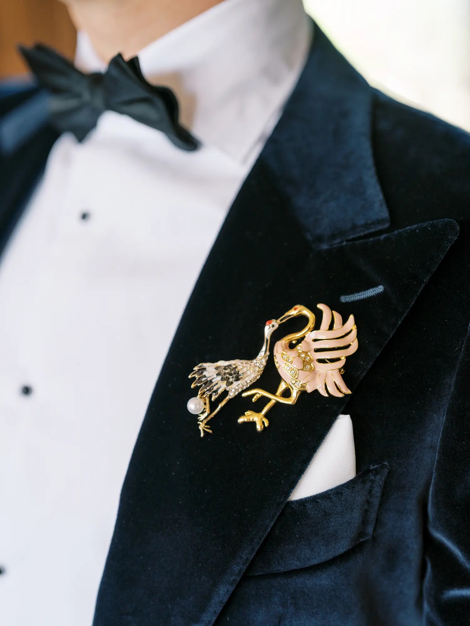 Vintage crystal crane and flamingo brooches in gold and pink enamel pinned to a navy velvet tuxedo lapel