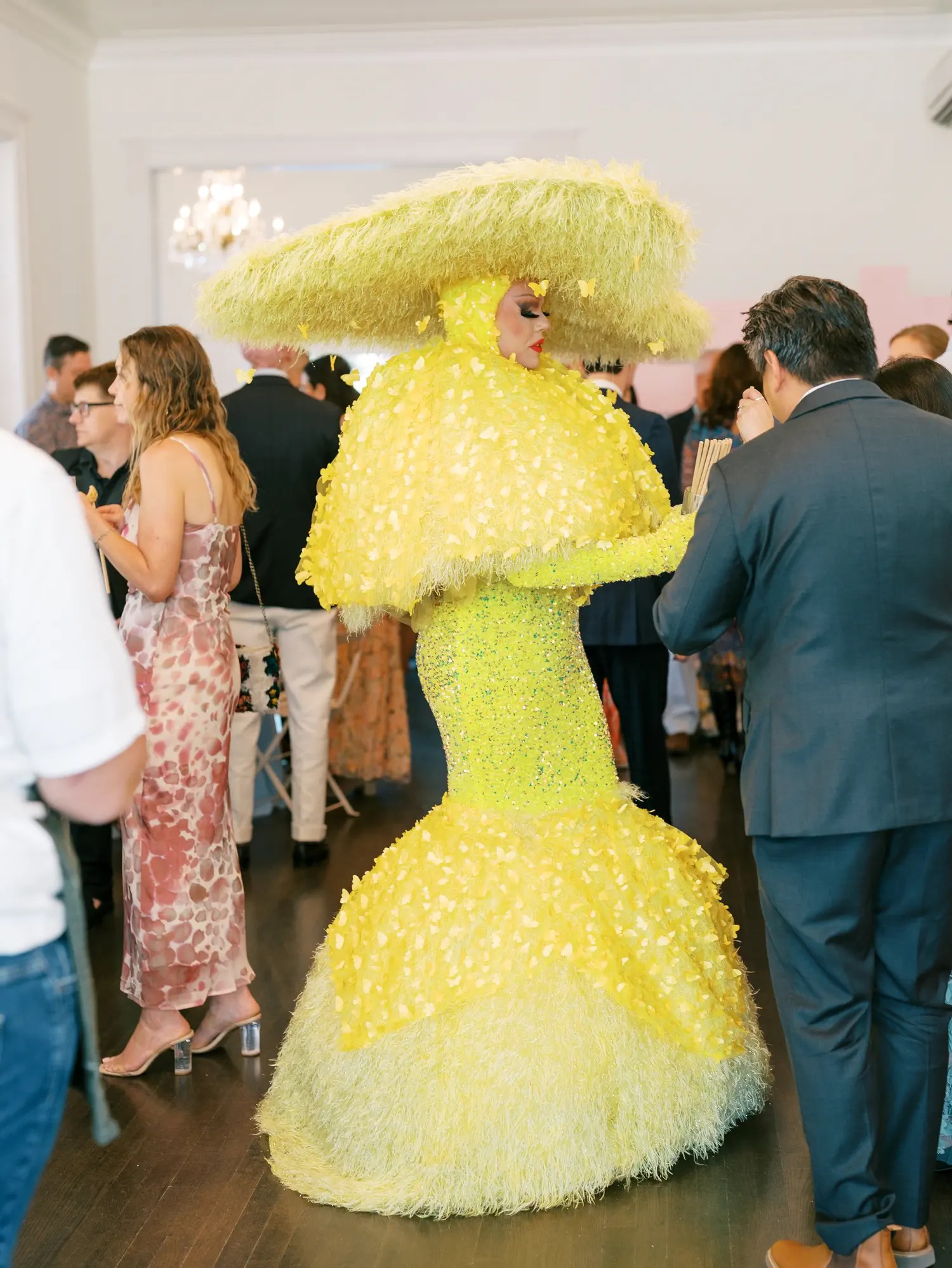 Drag performer in yellow sequin and petal gown with oversized fringe hat inside the mansion at a drag brunch wedding