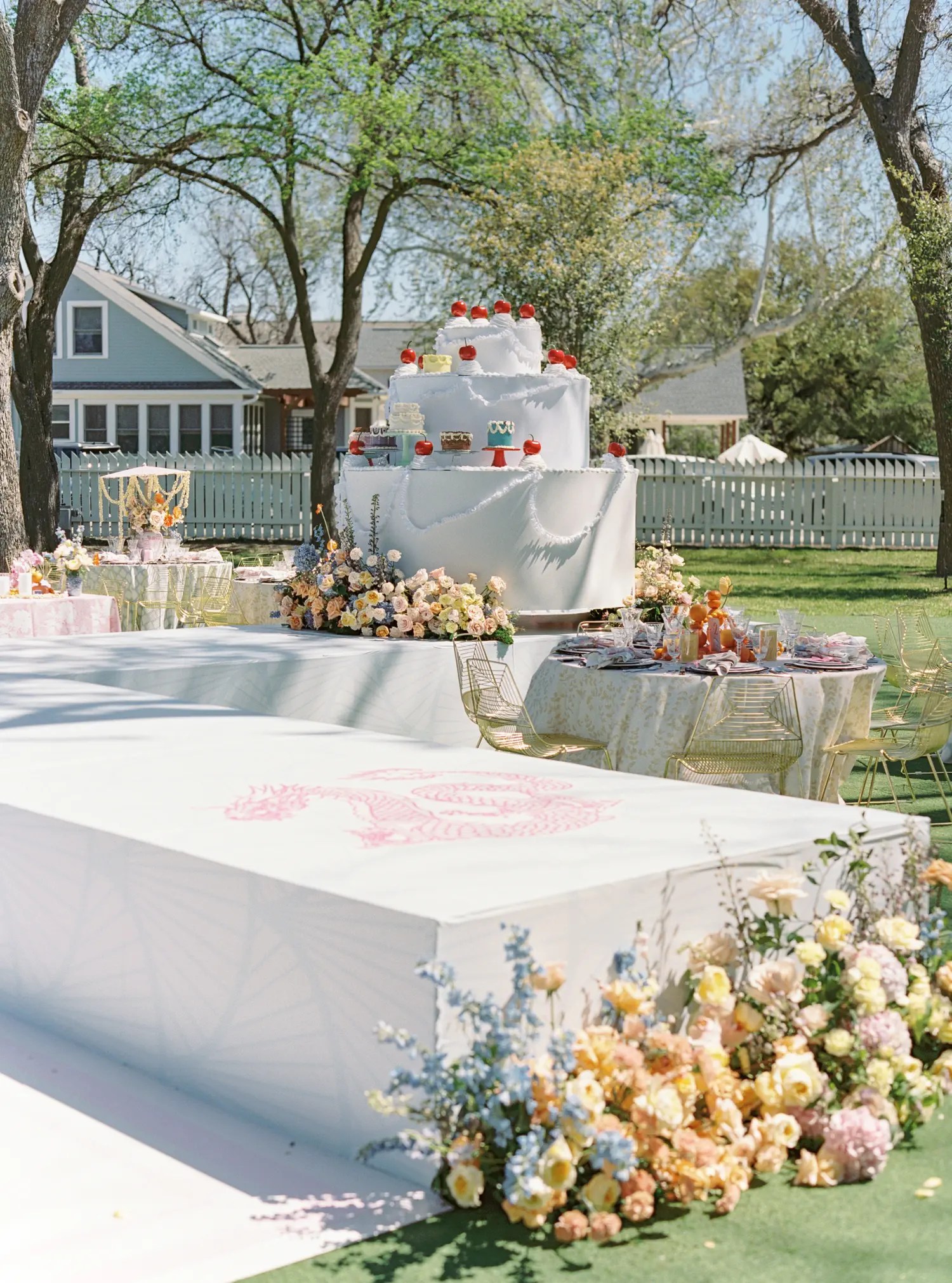 White dance floor runway leading to a giant tiered cake display with red cherry toppers and pastel flowers at the base