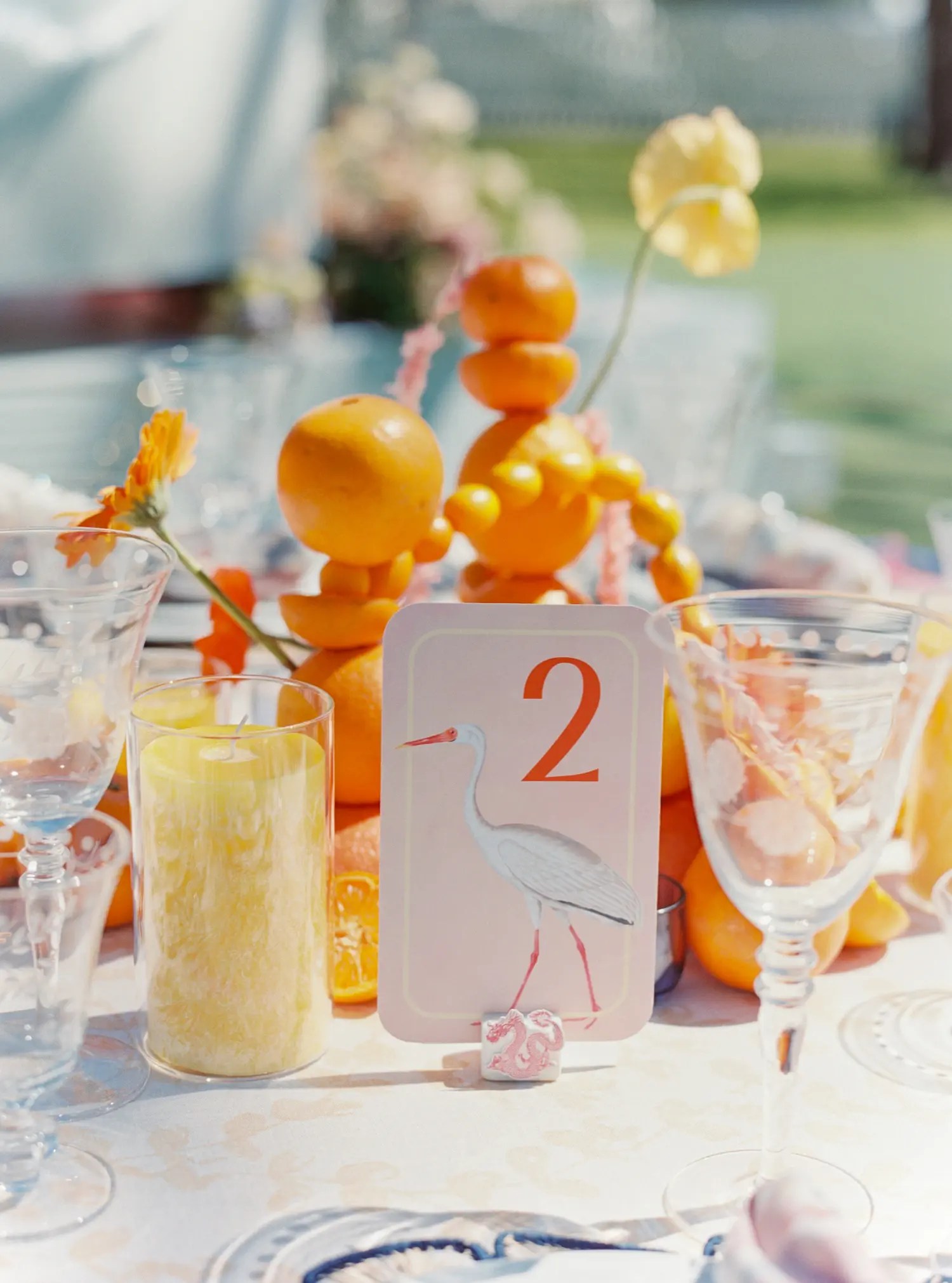 Heron-illustrated table number card in front of a stacked orange and tangerine centerpiece with a yellow pillar candle