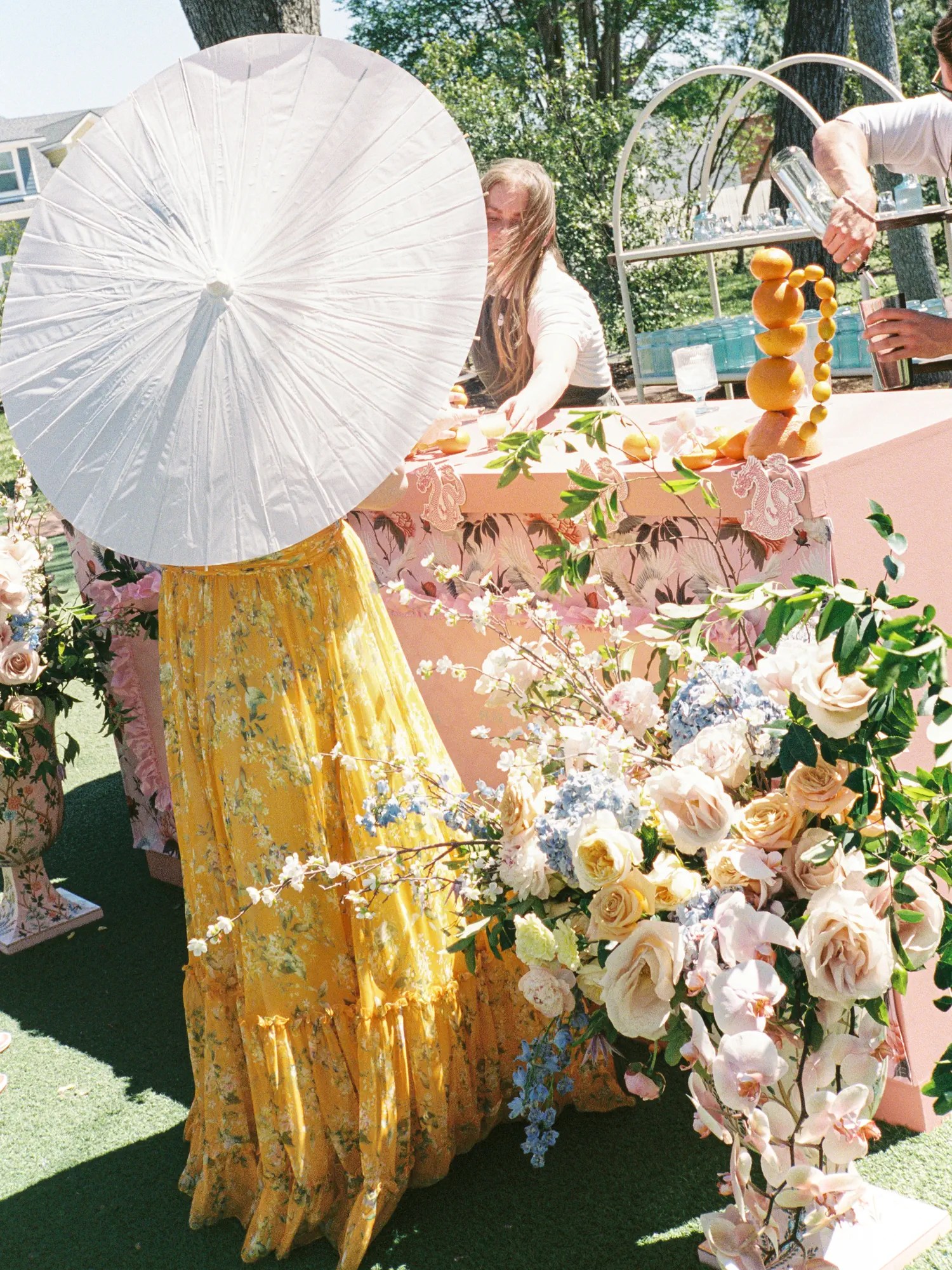 Guest in tiered yellow floral maxi skirt holding a white paper parasol at the crane-print wedding bar