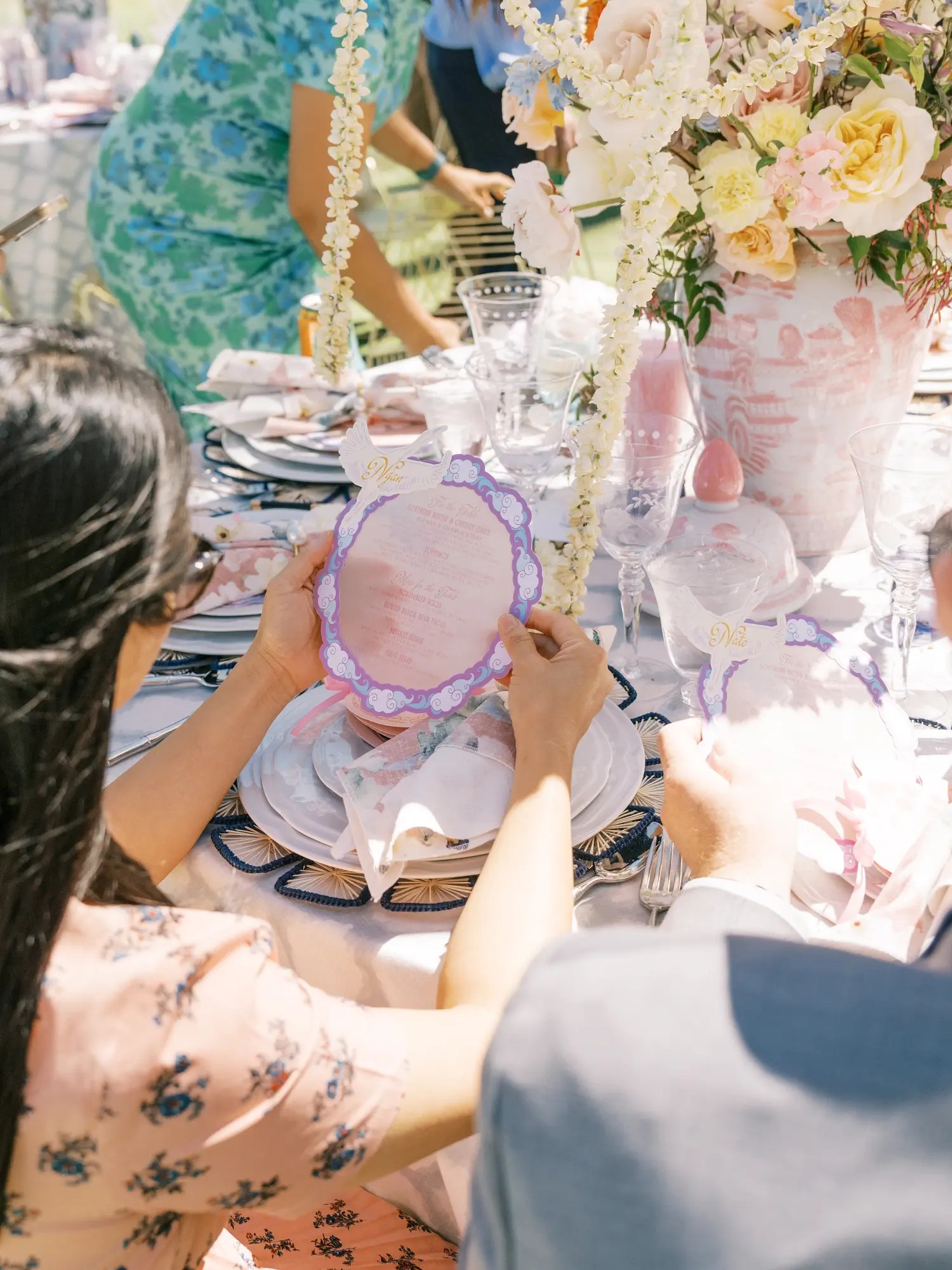 Guest in blush floral dress reading a scalloped lavender menu card at a brunch wedding reception table