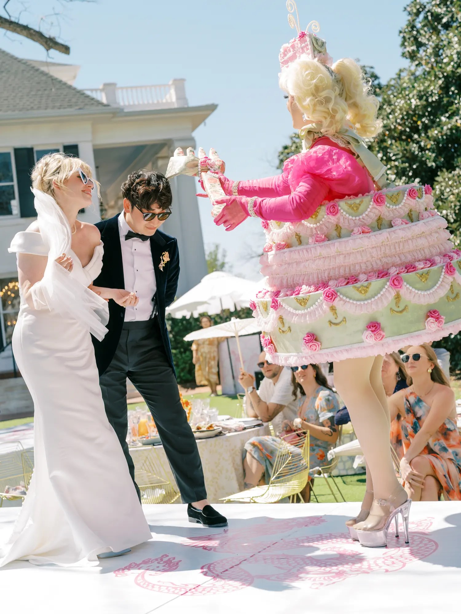 Drag queen in tiered wedding cake costume on stage with the laughing bride and groom at an Austin drag brunch wedding