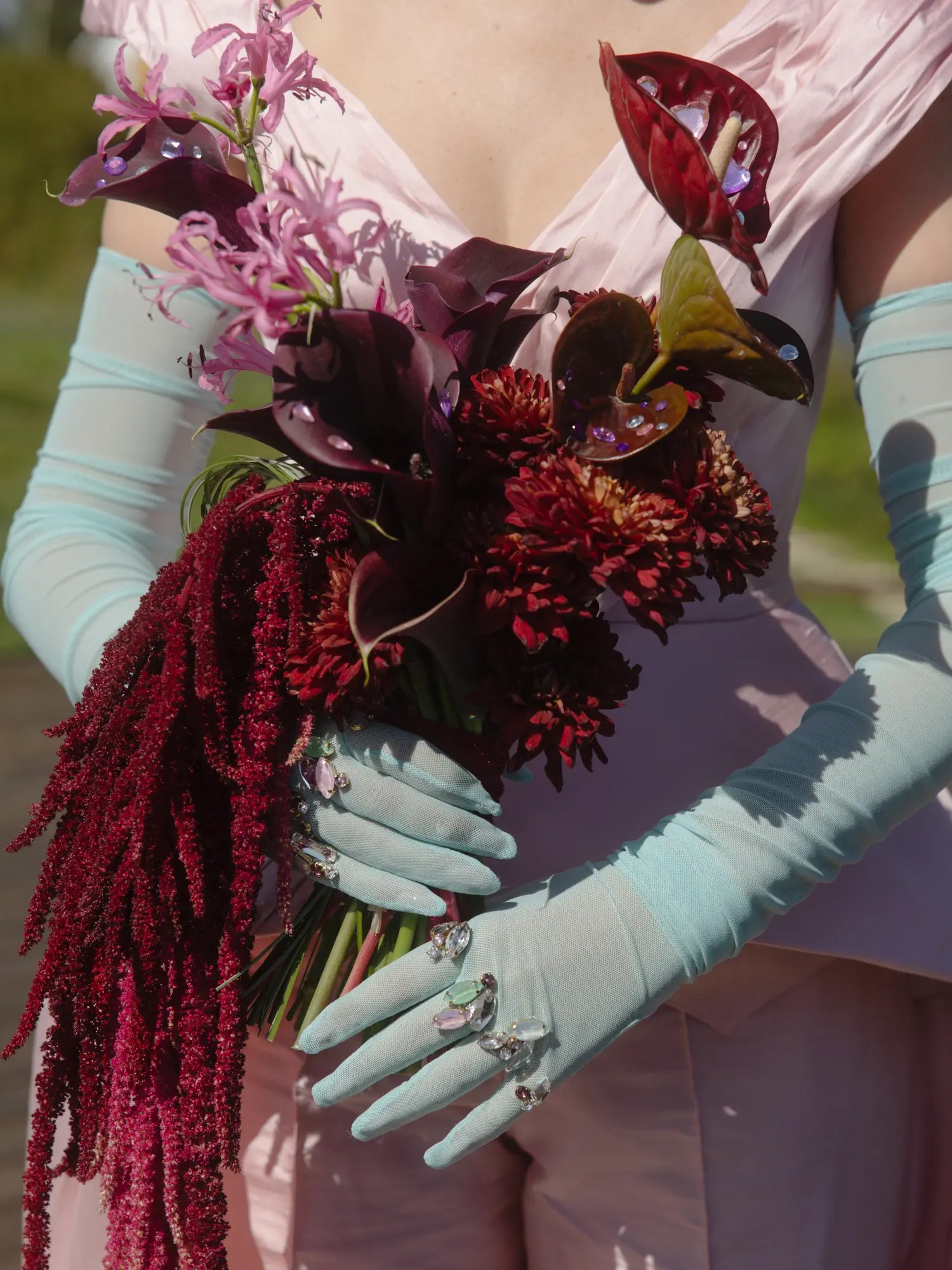 Faceted rhinestones dotted across sheer blue bridal gloves holding a dark calla lily bouquet with rhinestones and trailing amaranth