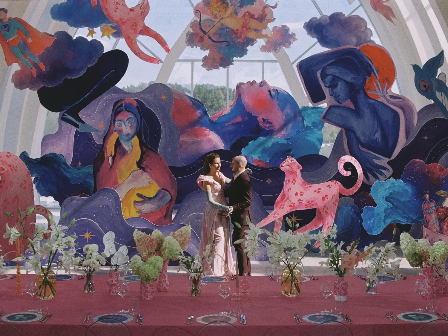 Couple holding hands before a towering indigo and hot pink illustrated mural behind a pink draped reception table