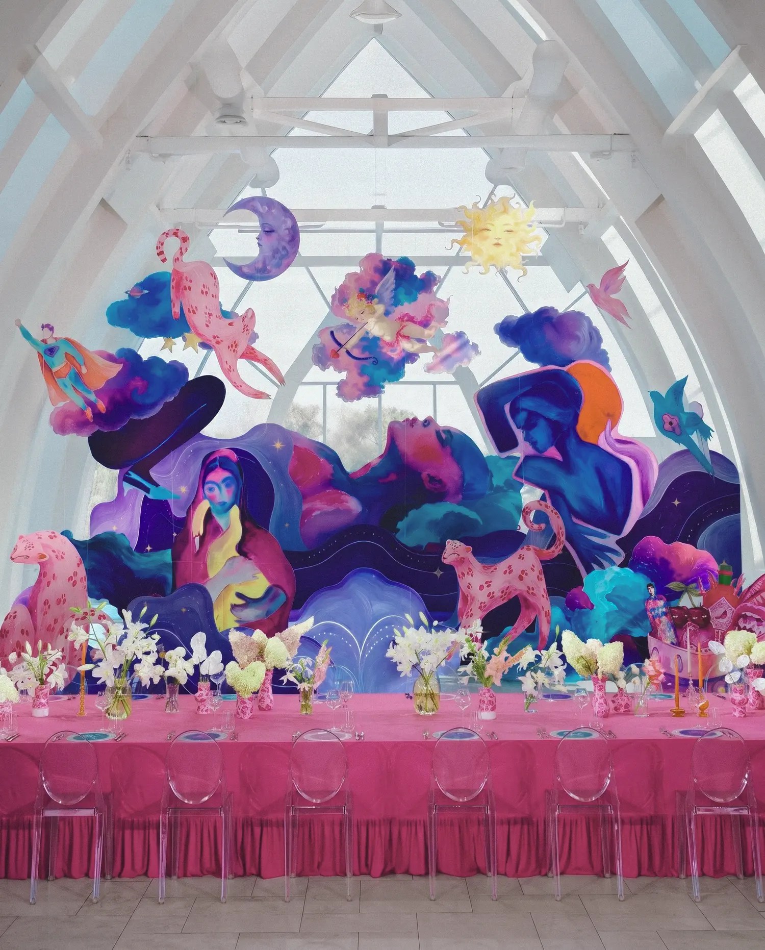 Glass-roofed reception hall with fantasy mural, pink leopard sculptures, hot pink banquet table and hanging moon, sun and cupid cut-outs