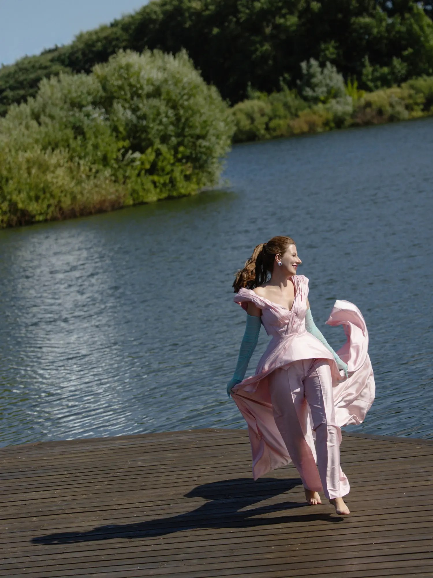 Bride spinning barefoot on a lakeside wooden dock with her blush pink satin gown blowing in the wind