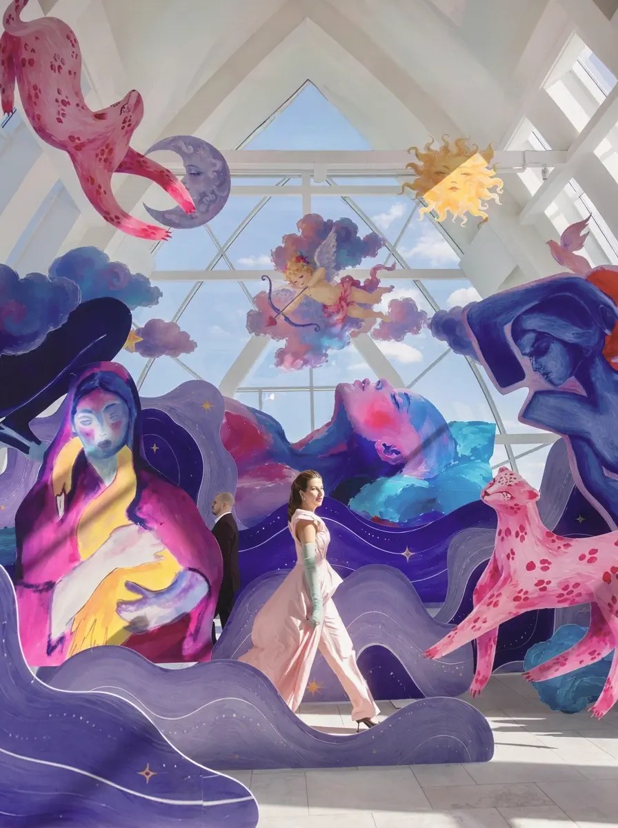 Bride in pale pink gown and mint green gloves walking through a hall of giant hand-painted mural figures and ceiling cut-outs
