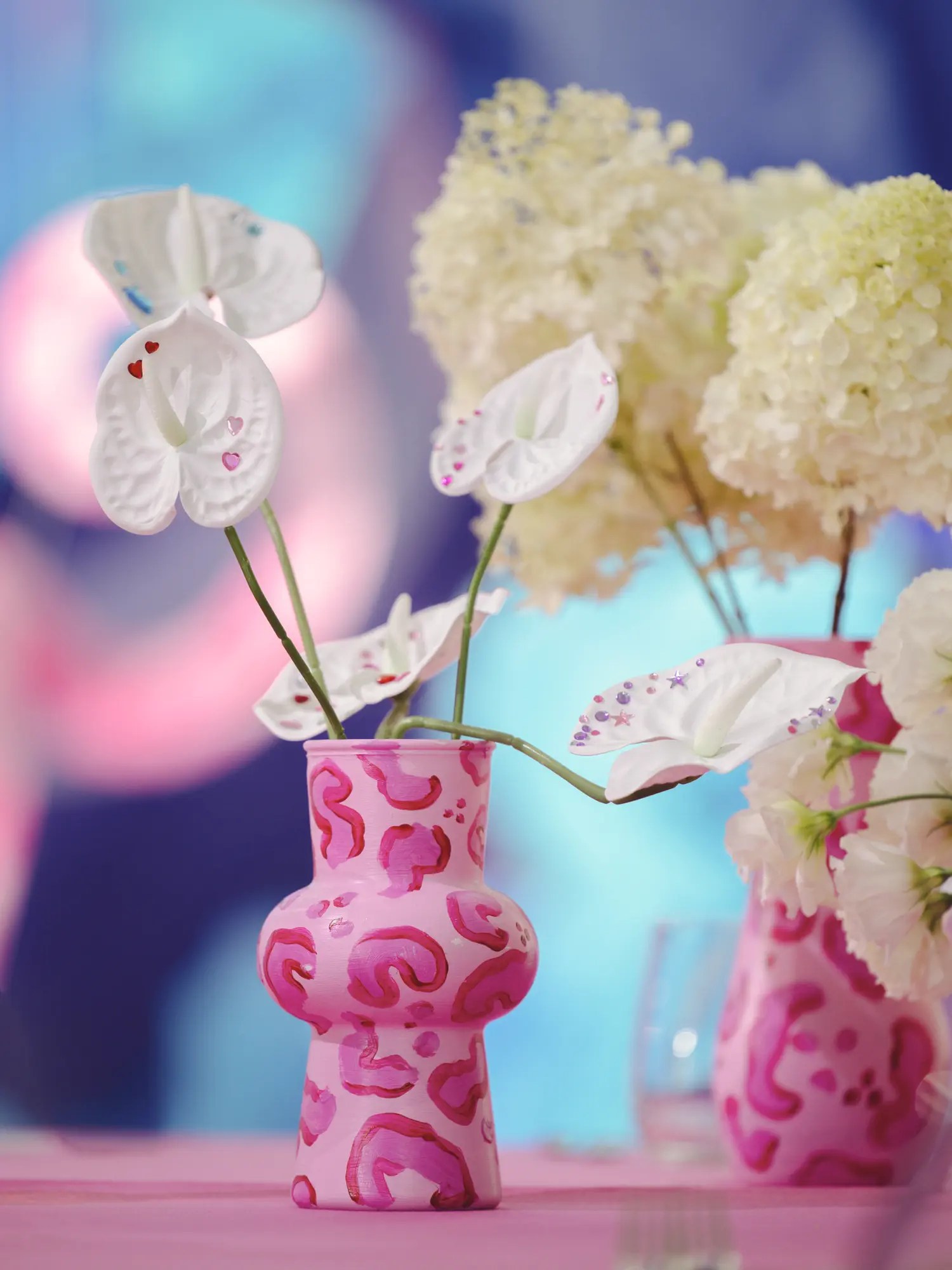 Hand-painted pink leopard print ceramic vases holding sticker-decorated white anthuriums and hydrangeas