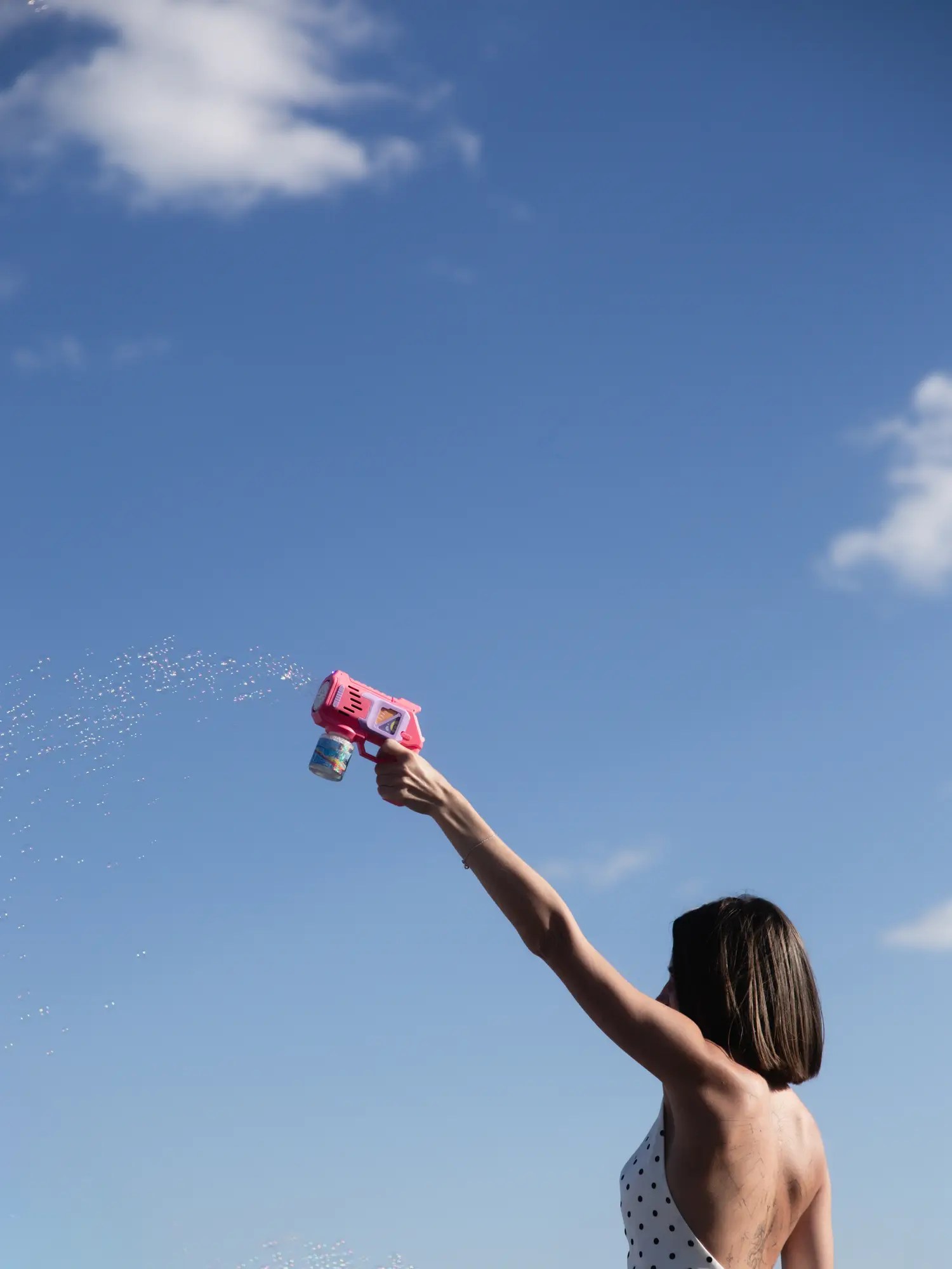 Arm raised against a blue sky firing a pink bubble gun during a wedding recessional