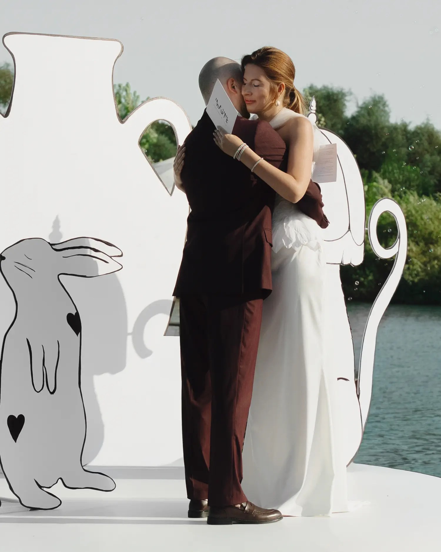 First kiss on a round white ceremony platform beside a white outlined rabbit cut-out with soap bubbles drifting in