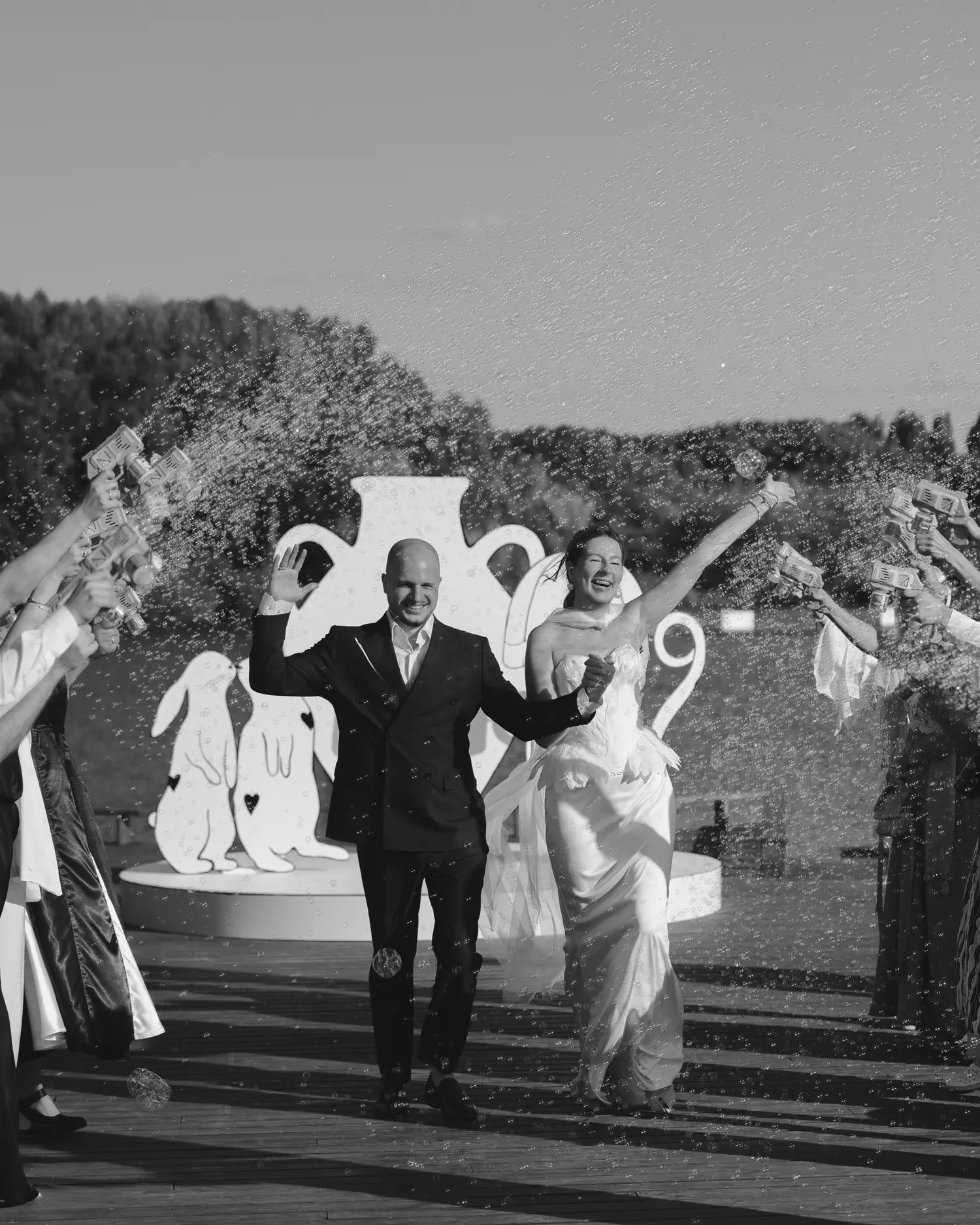 Black and white photo of a bubble-filled wedding recessional in front of a white graphic rabbit installation