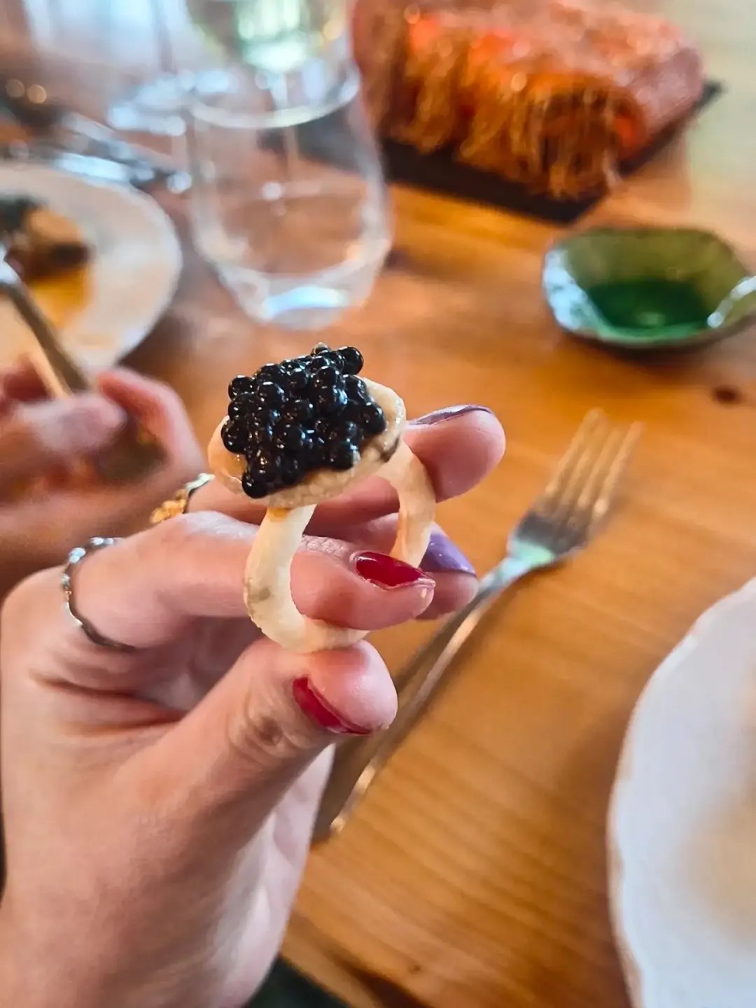 Hand with red nail polish holding a blini topped with black caviar and cream at a wedding grazing table