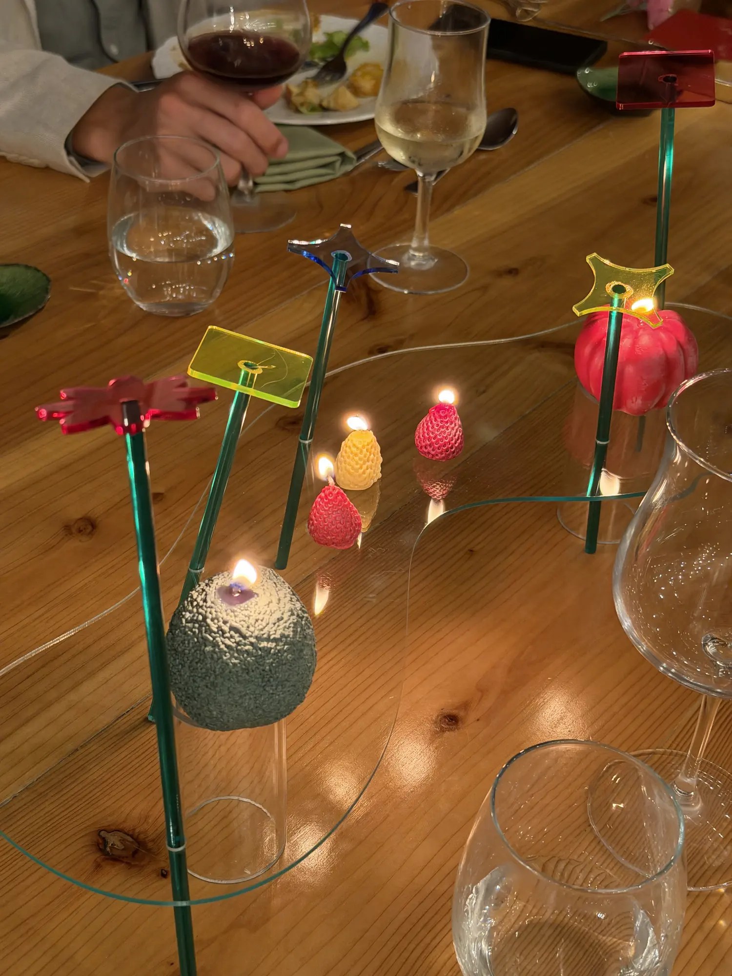 Acrylic Garden wedding centerpiece of green metal rods and colorful acrylic flowers with lit avocado, pinecone, strawberry, and tomato shaped candles