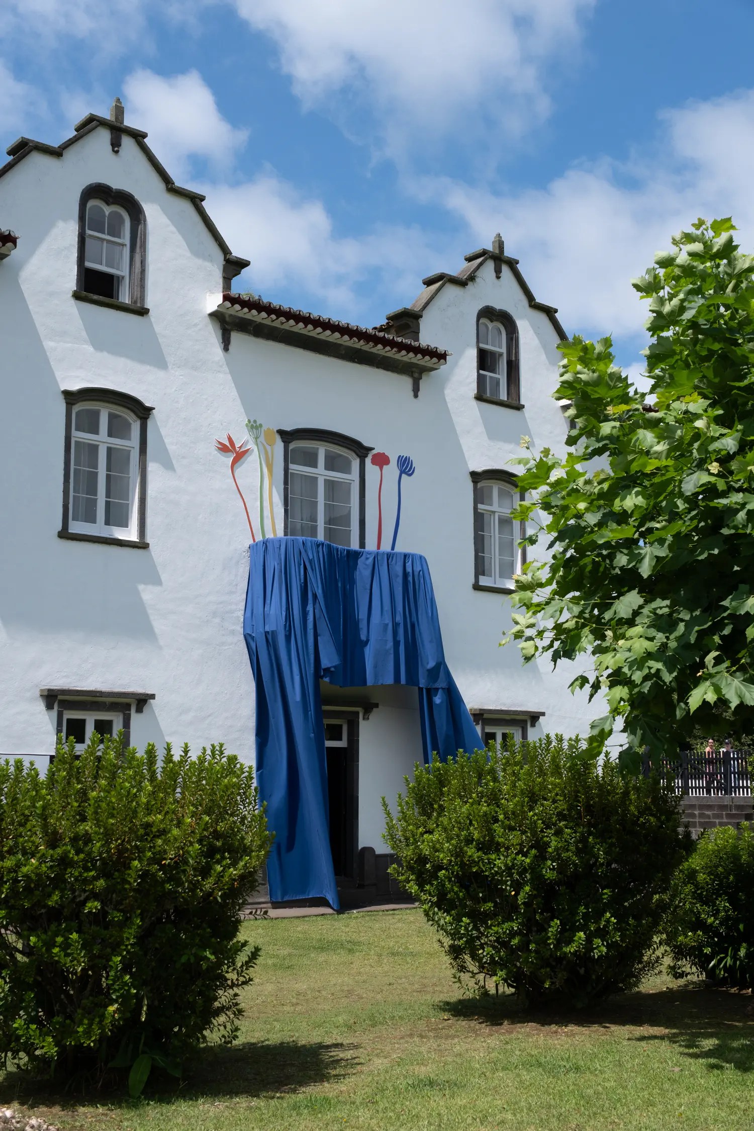 Casa Grande manor house in Sete Cidades with a cobalt blue fabric curtain draped over the entrance and colorful sculptural flower stems above the door