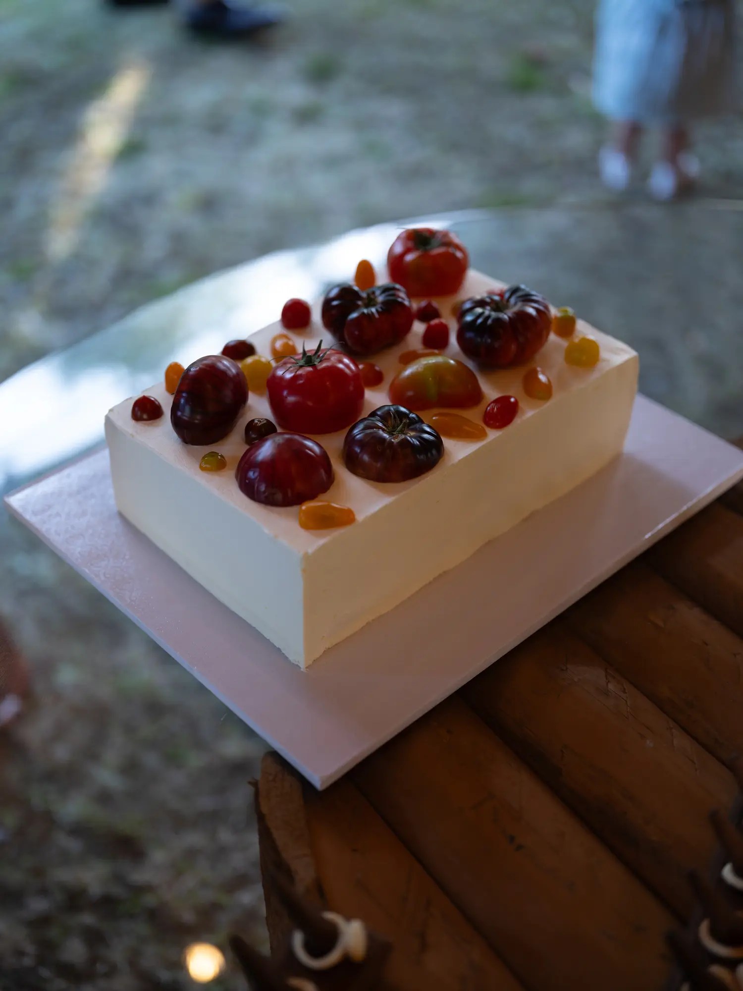 Two-tier savory smoked salmon wedding cake by Amori Cakes topped with heirloom and cherry tomatoes, on a pink board and wooden stump