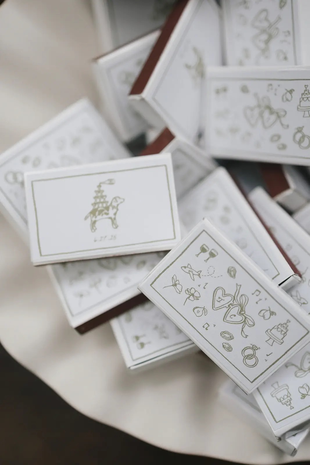 Cadeaux de mariage personnalisés en forme de boîte d'allumettes blanches avec des coeurs, des bagues, des gâteaux et des notes de musique illustrés en or empilés sur une surface blanche