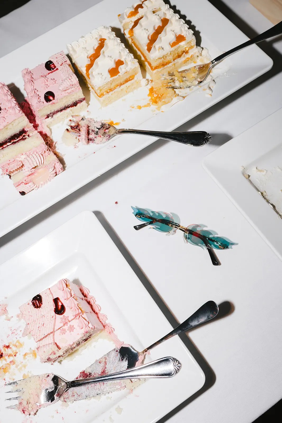 Vue aérienne de tranches de gâteau de mariage roses et blanches de Paper Cake Shop sur des assiettes blanches avec des lunettes de soleil teintées sans monture sur la table