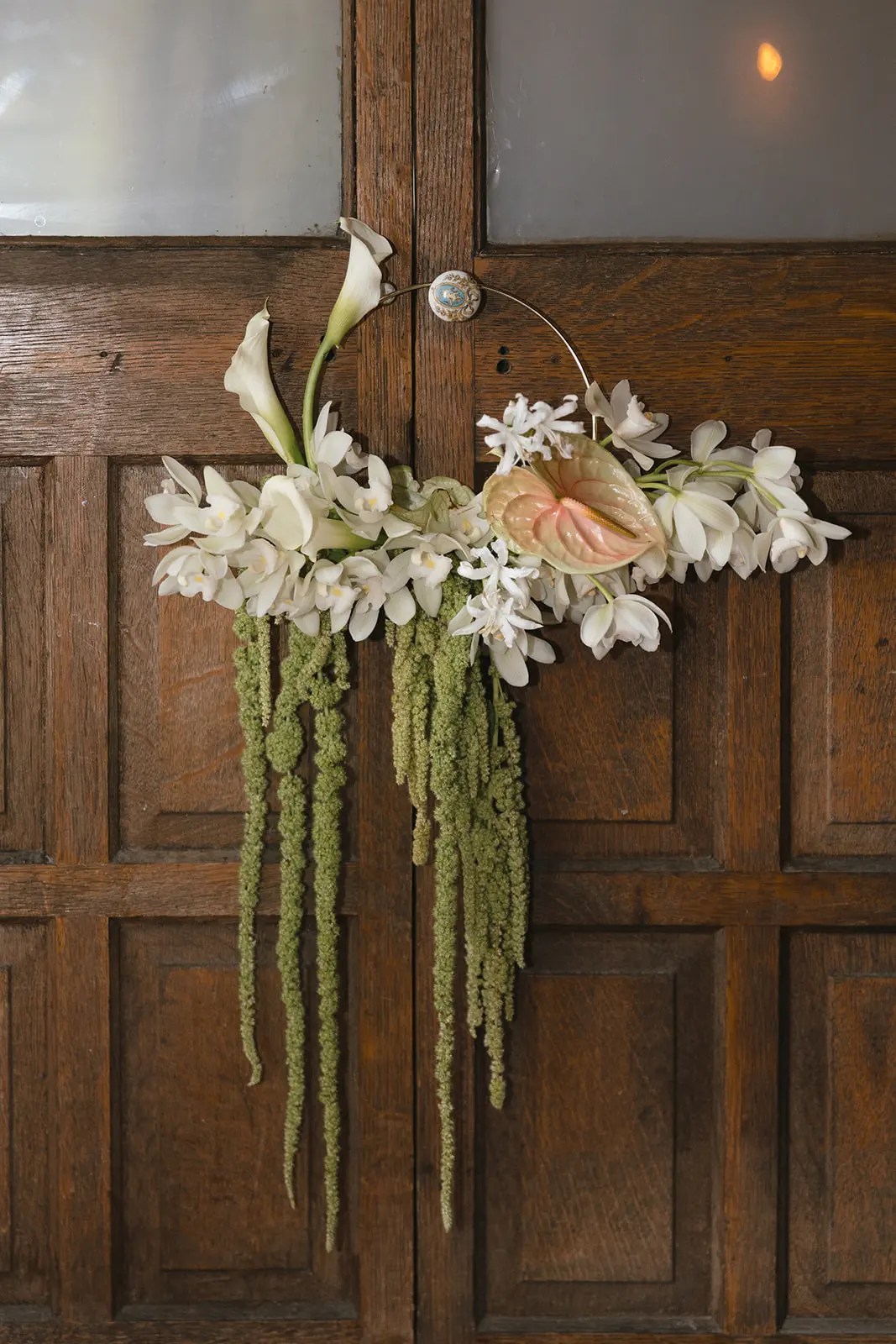 Sac à main avec bouquet floral par Kylie Hale Designs d'orchidées blanches, de lys calla, d'anthurium blush et d'amarante verte traînante accrochés à des portes doubles en noyer